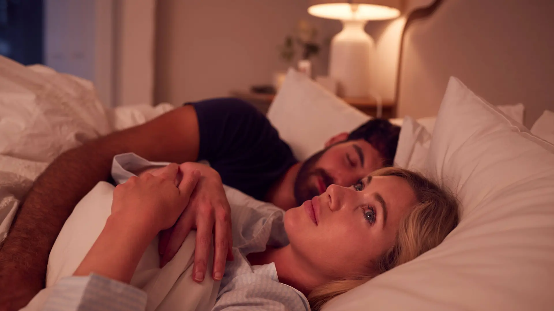 Frau liegt schlaflos im Bett neben ihrem schlafenden Partner.
