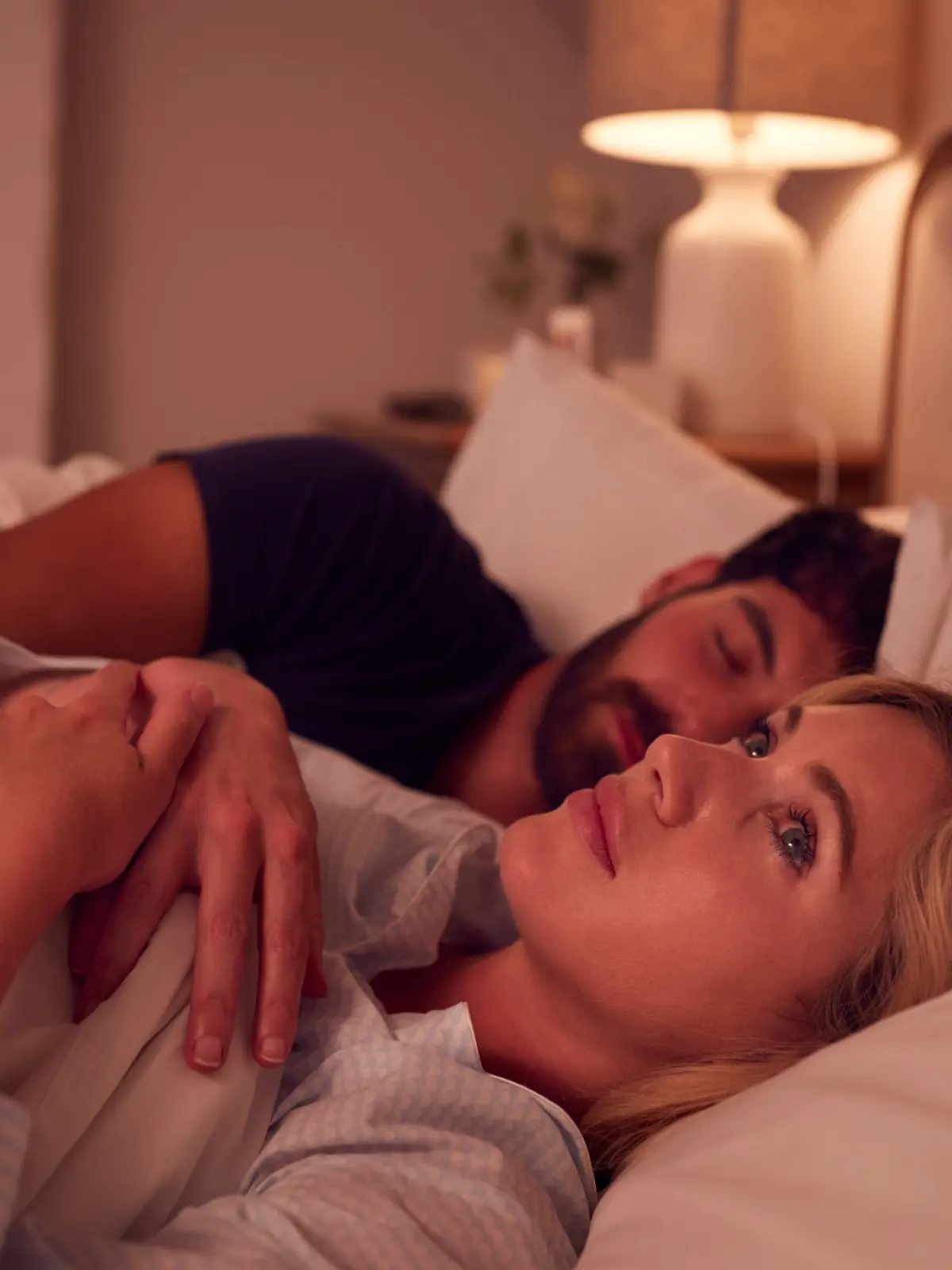 Frau liegt schlaflos im Bett neben ihrem schlafenden Partner.