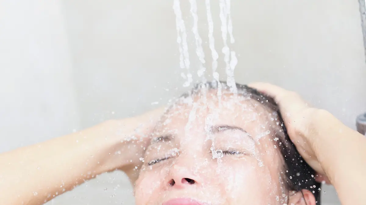 Shower woman washing face and hair smiling happy showering under shower head. Beautiful young joyful mixed race female model in bathroom at home.