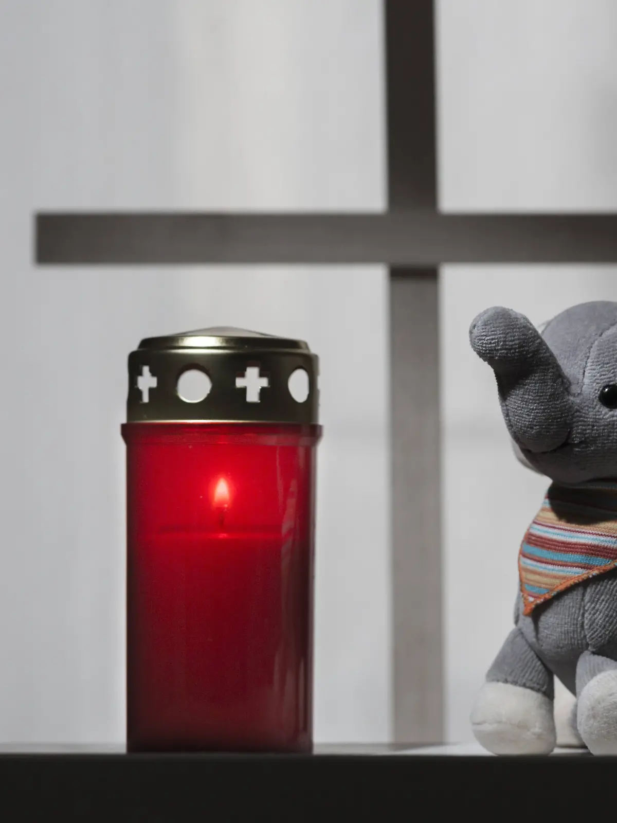 Grabkerze neben Stofftier mit einem Kreuz im Hintergrund.