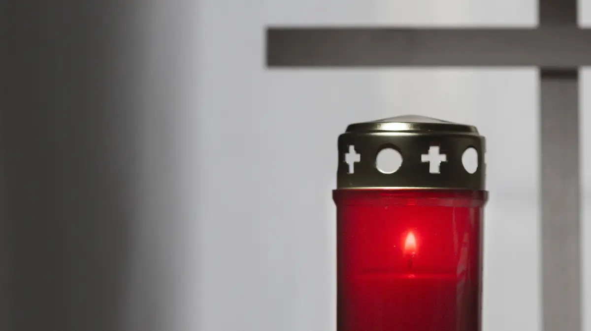 Grabkerze neben Stofftier mit einem Kreuz im Hintergrund.