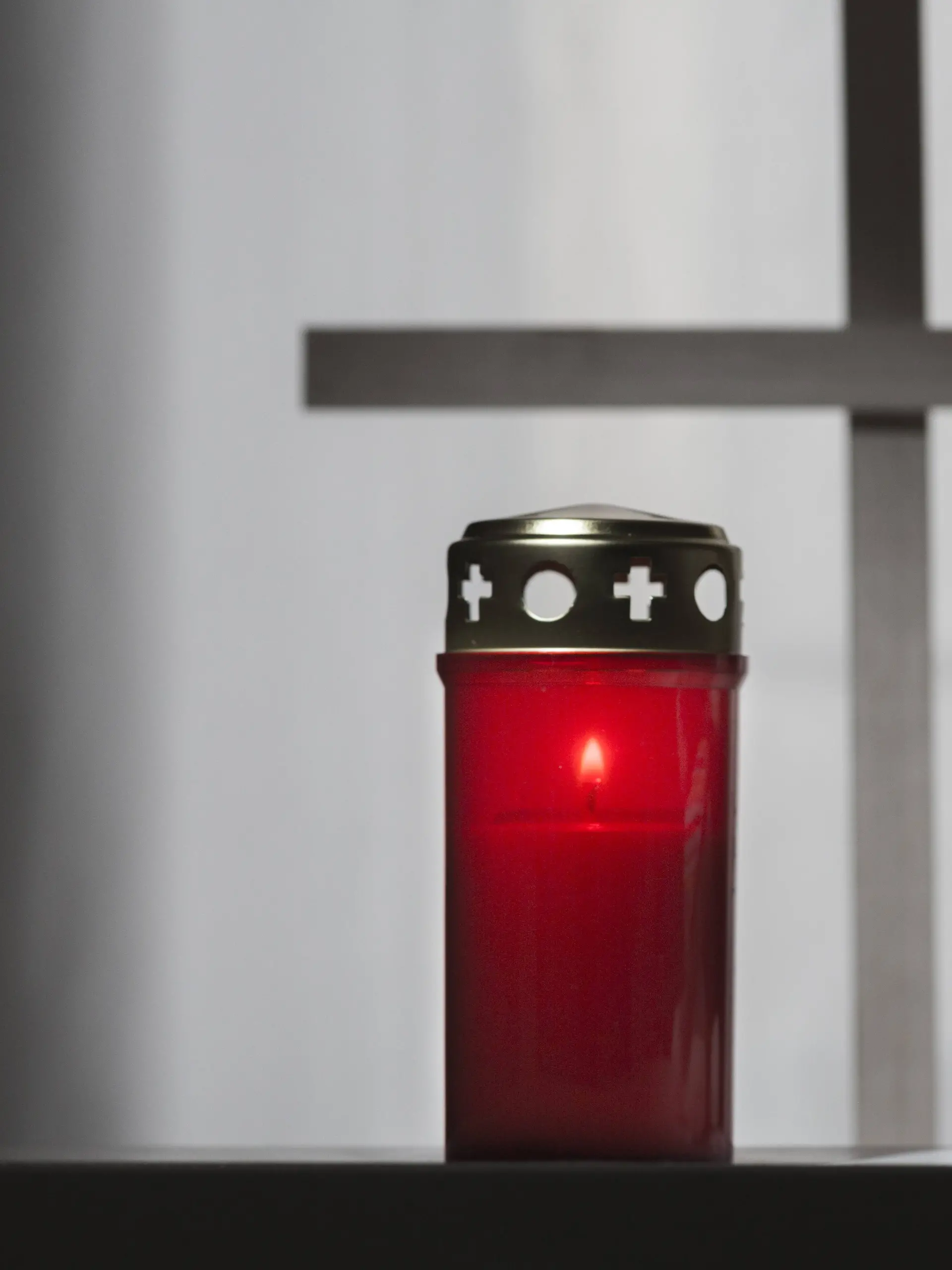 Grabkerze neben Stofftier mit einem Kreuz im Hintergrund.