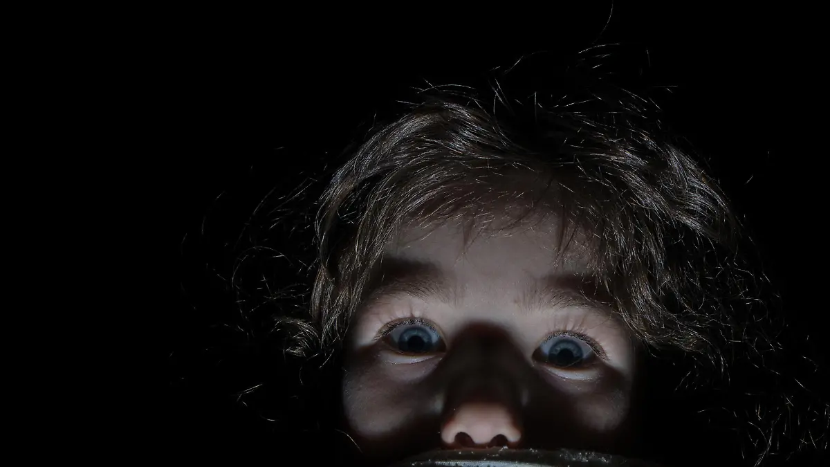 Headshot of little girl afraid and hiding behind her bed sheets