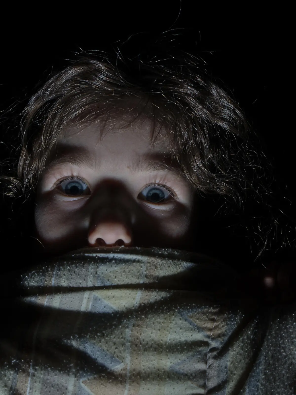 Headshot of little girl afraid and hiding behind her bed sheets