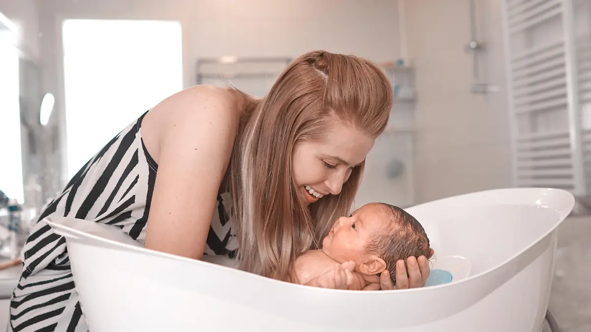 Junge Mutter badet lächelndes Baby in der Badewanne