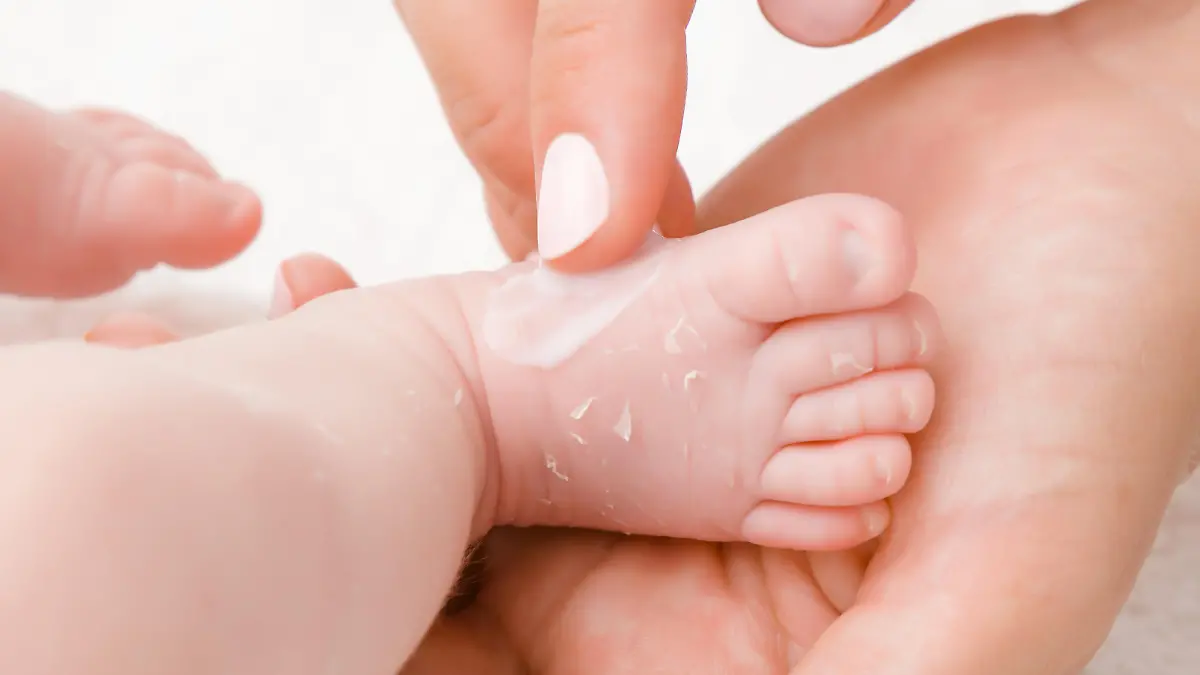 Mutter trägt Creme auf trockene Babyhaut auf