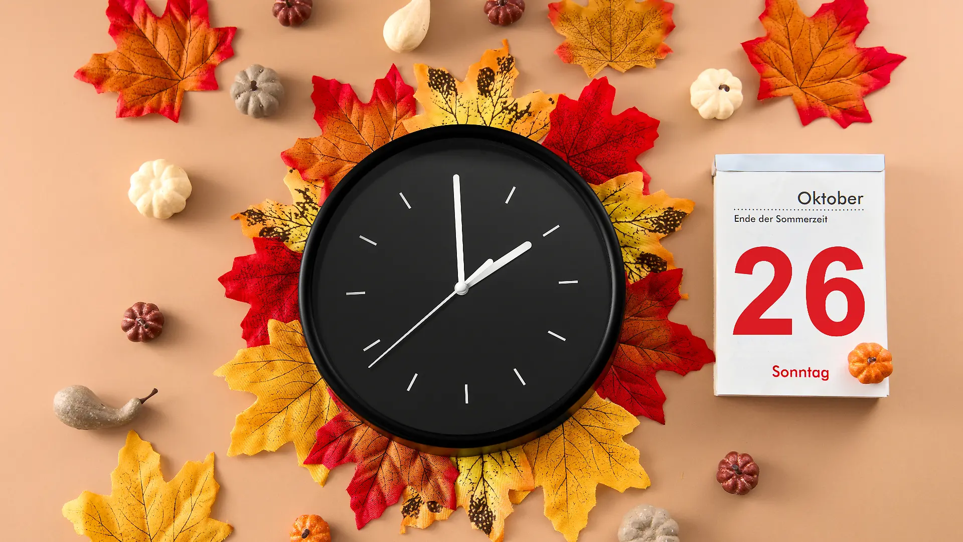 Uhr liegend auf Herbst-Blättern sowie einem Kalender daneben, der den Tag der Zeitumstellung, 26. Oktober, verrät