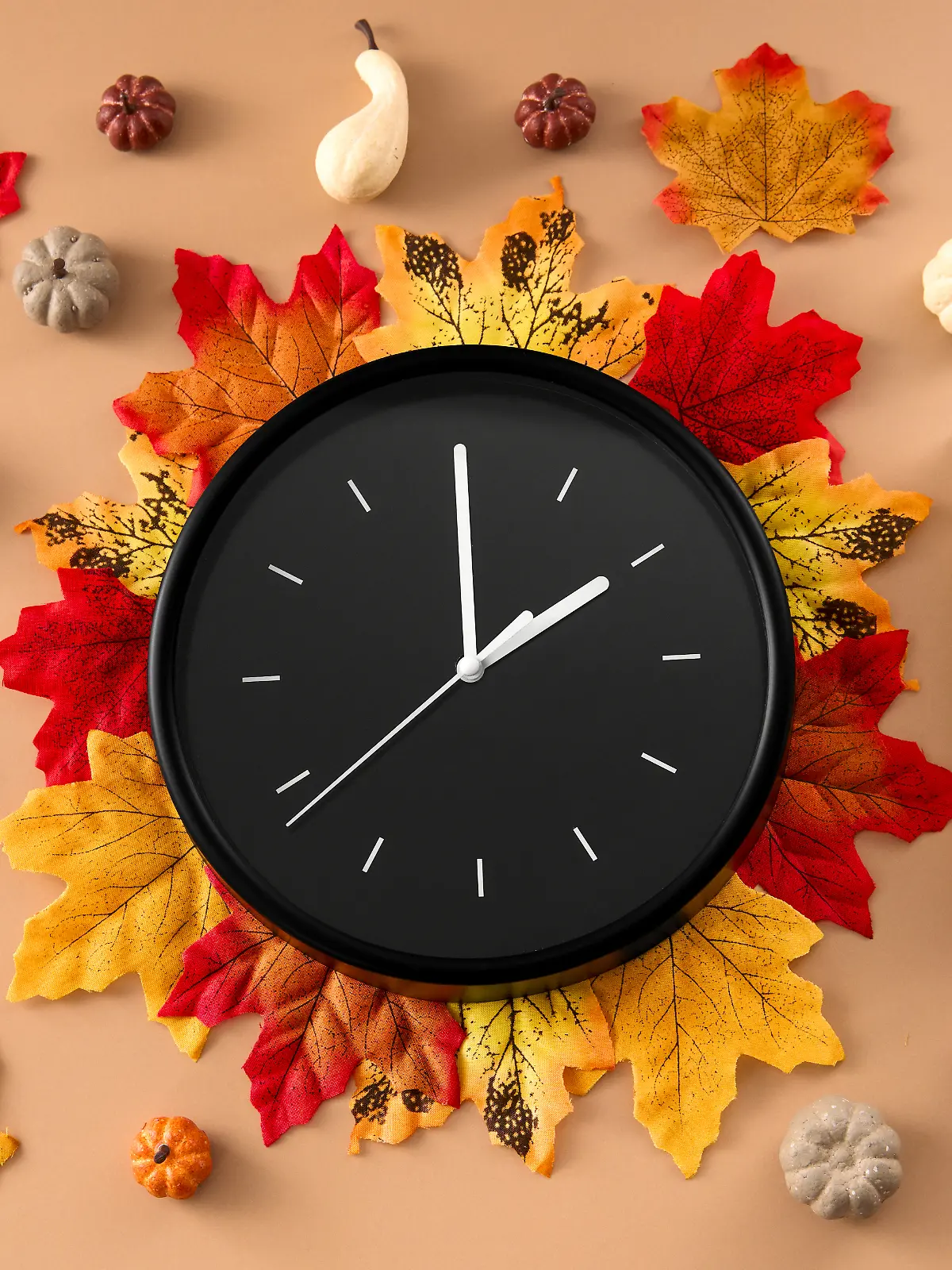 Uhr liegend auf Herbst-Blättern sowie einem Kalender daneben, der den Tag der Zeitumstellung, 26. Oktober, verrät