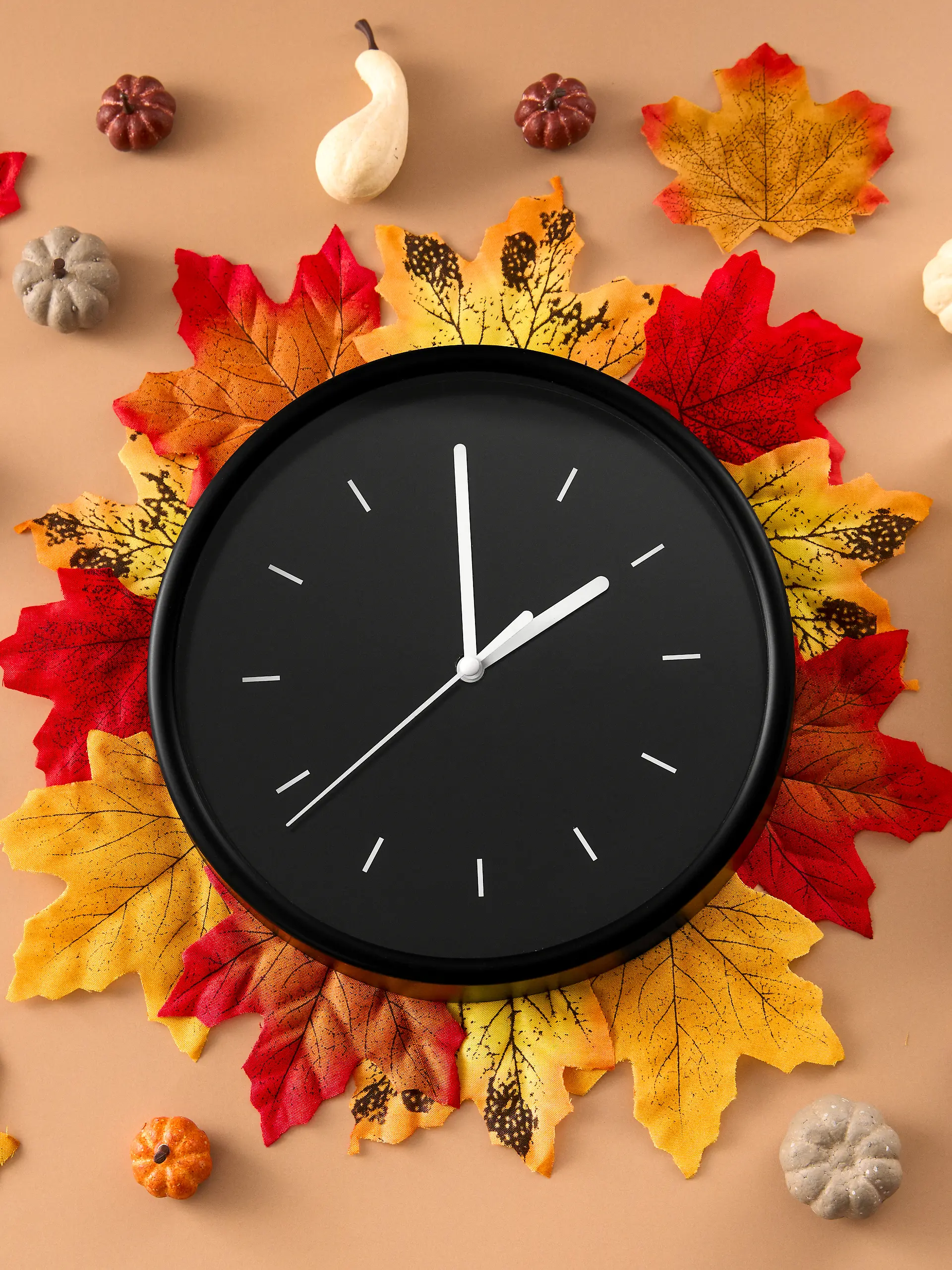 Uhr liegend auf Herbst-Blättern sowie einem Kalender daneben, der den Tag der Zeitumstellung, 26. Oktober, verrät