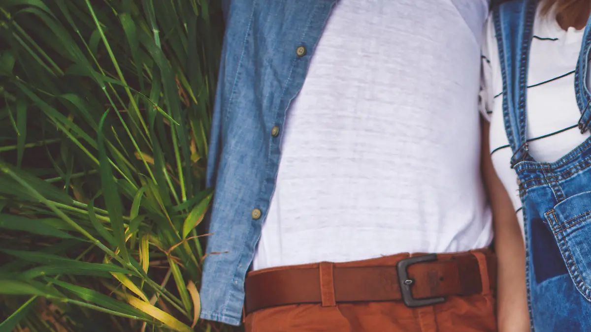 Photo of a young couple, soon to become parents, resting in the middle of the field on a beautiful spring day while expecting a new life to begin. Baby bump is in a focus, while parents are out of the frame