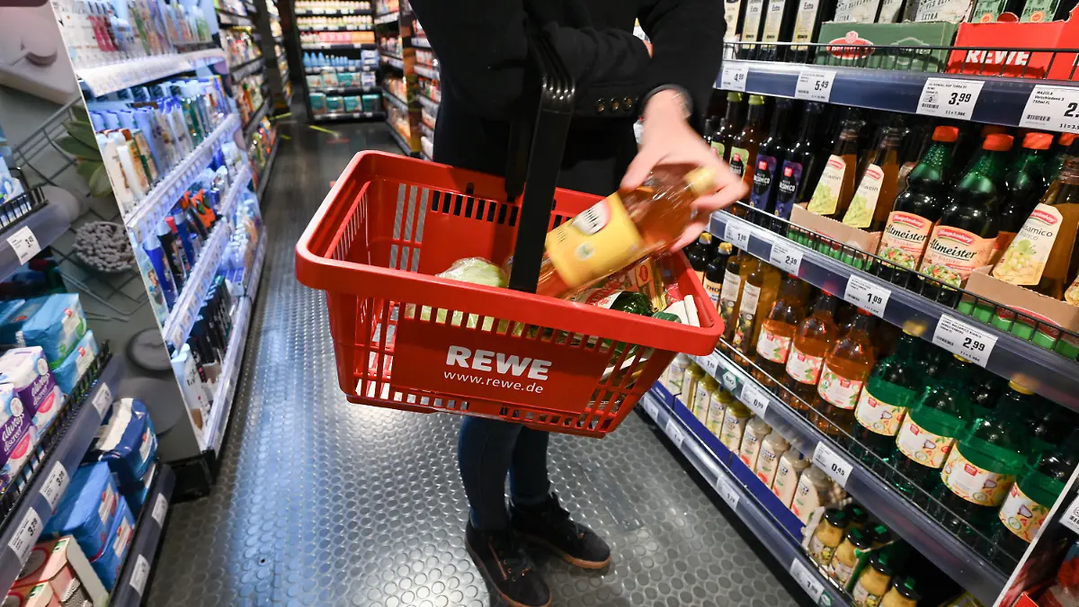 ARCHIV - 05.11.2021, Hessen, Frankfurt/Main: Eine Frau steht bei der Vorstellung des temporären Projekts "Fairer Supermarkt im Zug" im Frankfurter Hauptbahnhof mit einem Einkaufskorb vor einem Lebensmittelregal. Bereits im Jahr 2022 habe Rewe durch hartes Verhandeln die Umsetzung von mehr als der Hälfte der Preisforderungen der Hersteller verhindert. (zu dpa "Rewe: Markenartikler fordern Preisanhebungen in Milliardenhöhe") Foto: Arne Dedert/dpa +++ dpa-Bildfunk +++