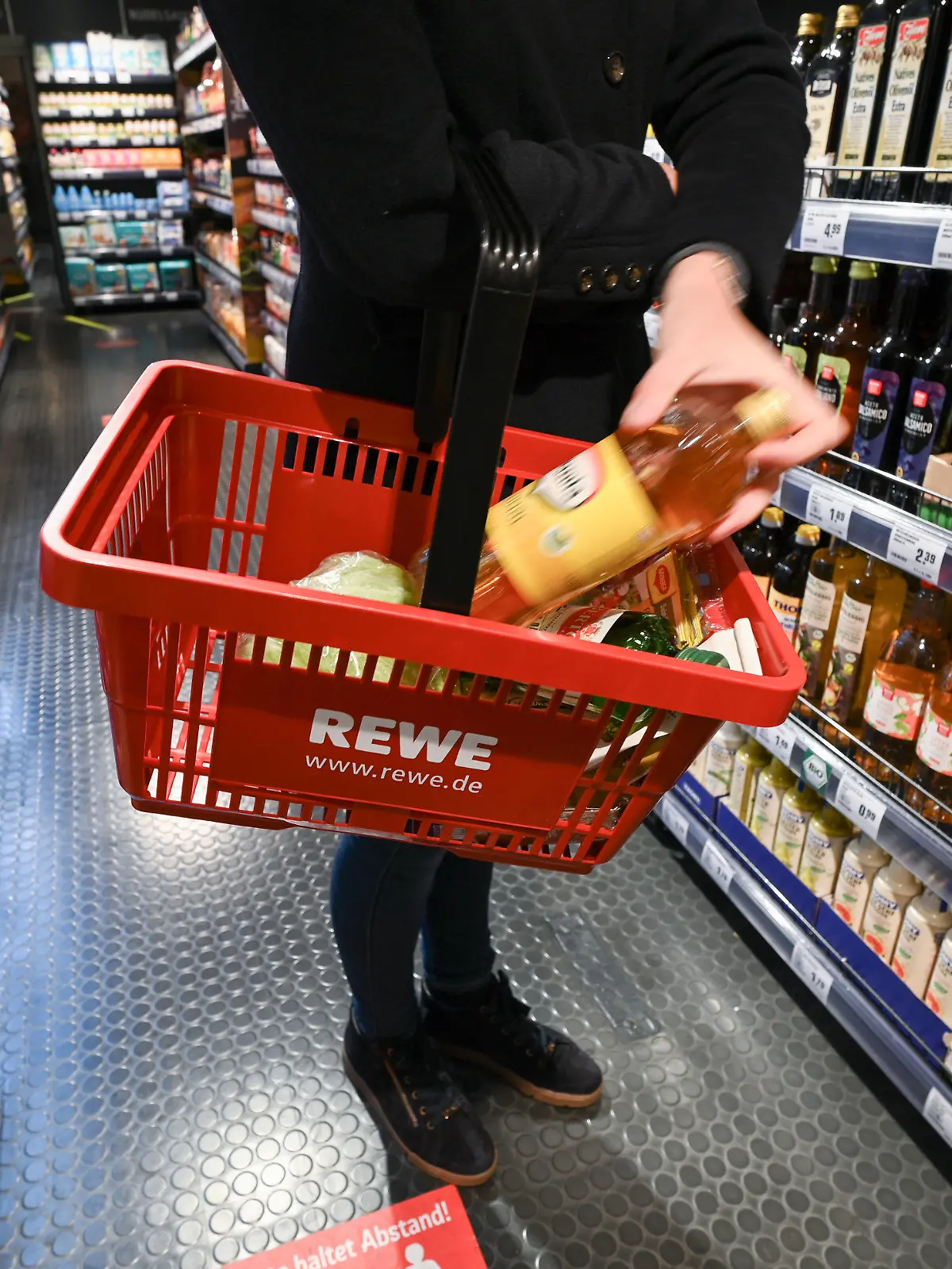 ARCHIV - 05.11.2021, Hessen, Frankfurt/Main: Eine Frau steht bei der Vorstellung des temporären Projekts "Fairer Supermarkt im Zug" im Frankfurter Hauptbahnhof mit einem Einkaufskorb vor einem Lebensmittelregal.  Bereits im Jahr 2022 habe Rewe durch hartes Verhandeln die Umsetzung von mehr als der Hälfte der Preisforderungen der Hersteller verhindert. (zu dpa "Rewe: Markenartikler fordern Preisanhebungen in Milliardenhöhe") Foto: Arne Dedert/dpa +++ dpa-Bildfunk +++