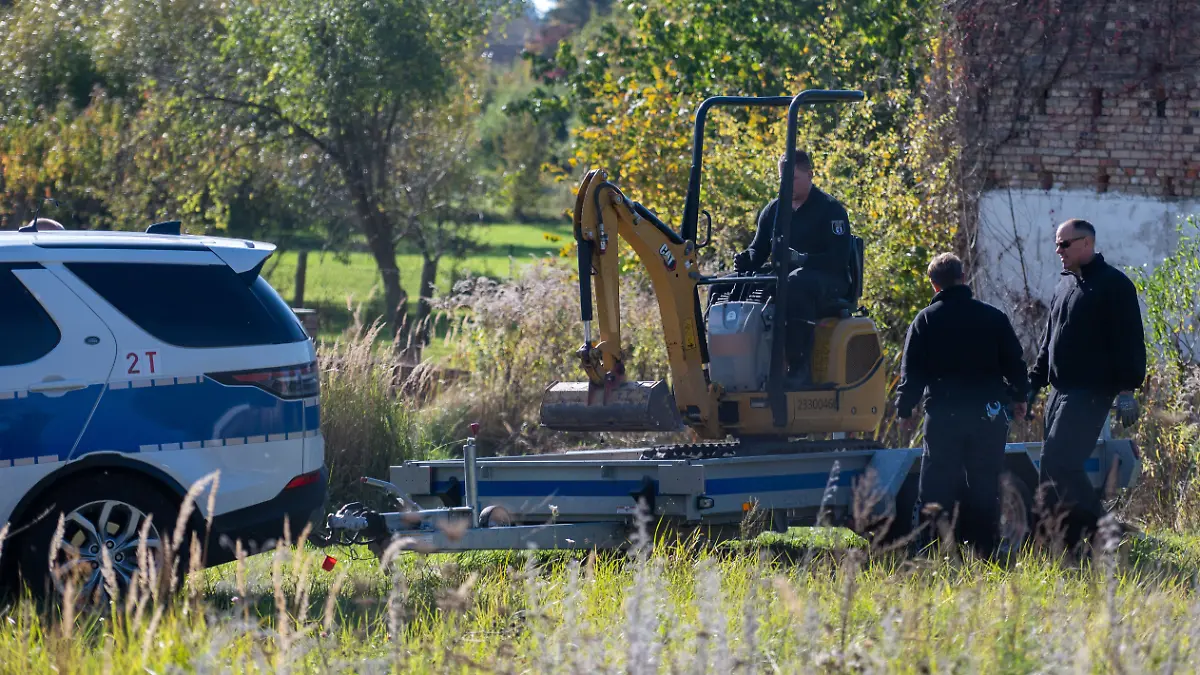 Polizisten untersuchen mit einem Bagger ein Grundstück in Tauche