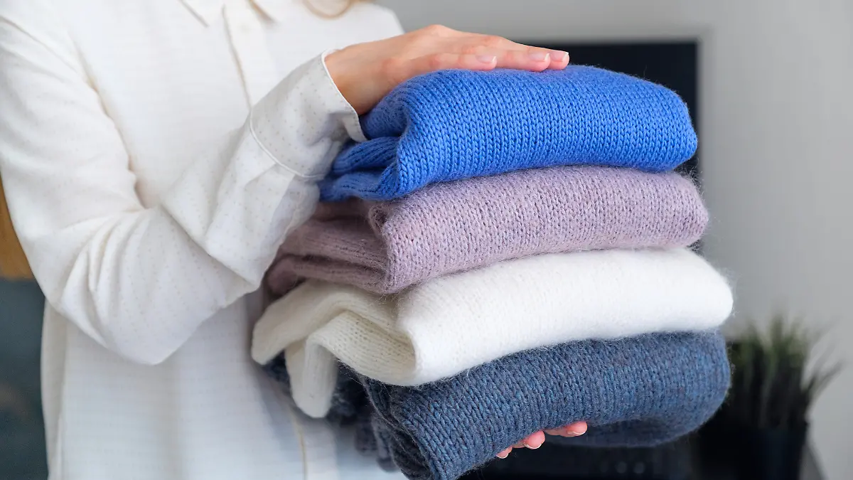 Frau trägt eine Bluse und hält verschieden farbige Pullover in der Hand.