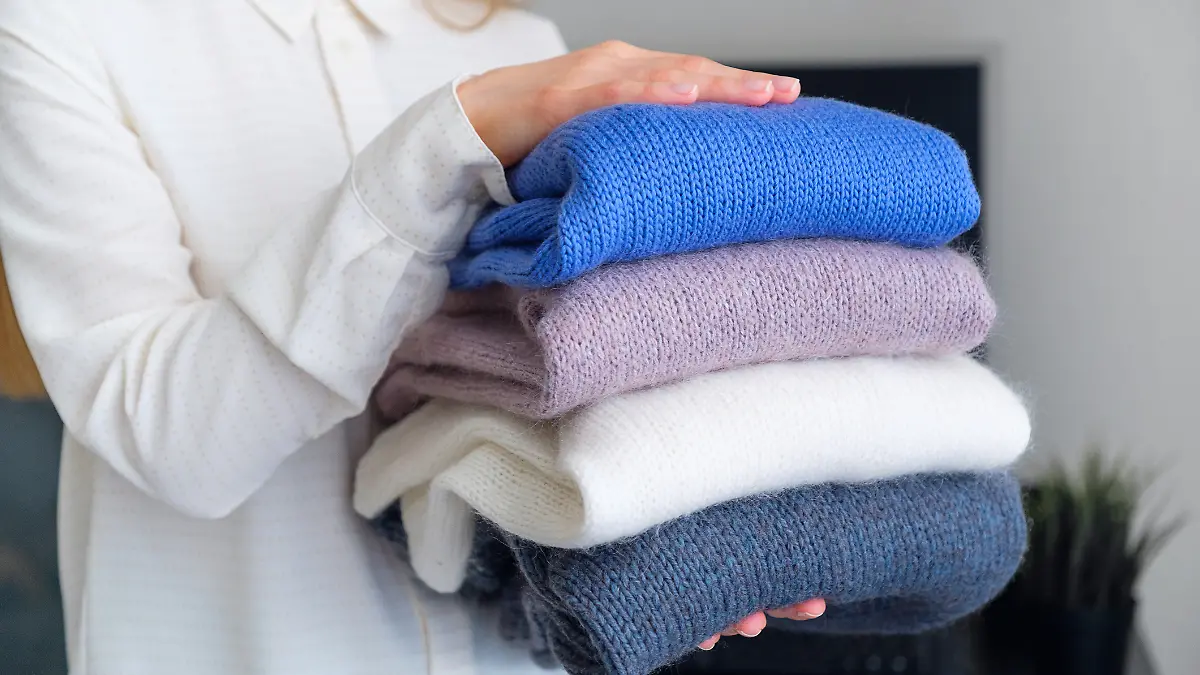 Frau trägt eine Bluse und hält verschieden farbige Pullover in der Hand. 