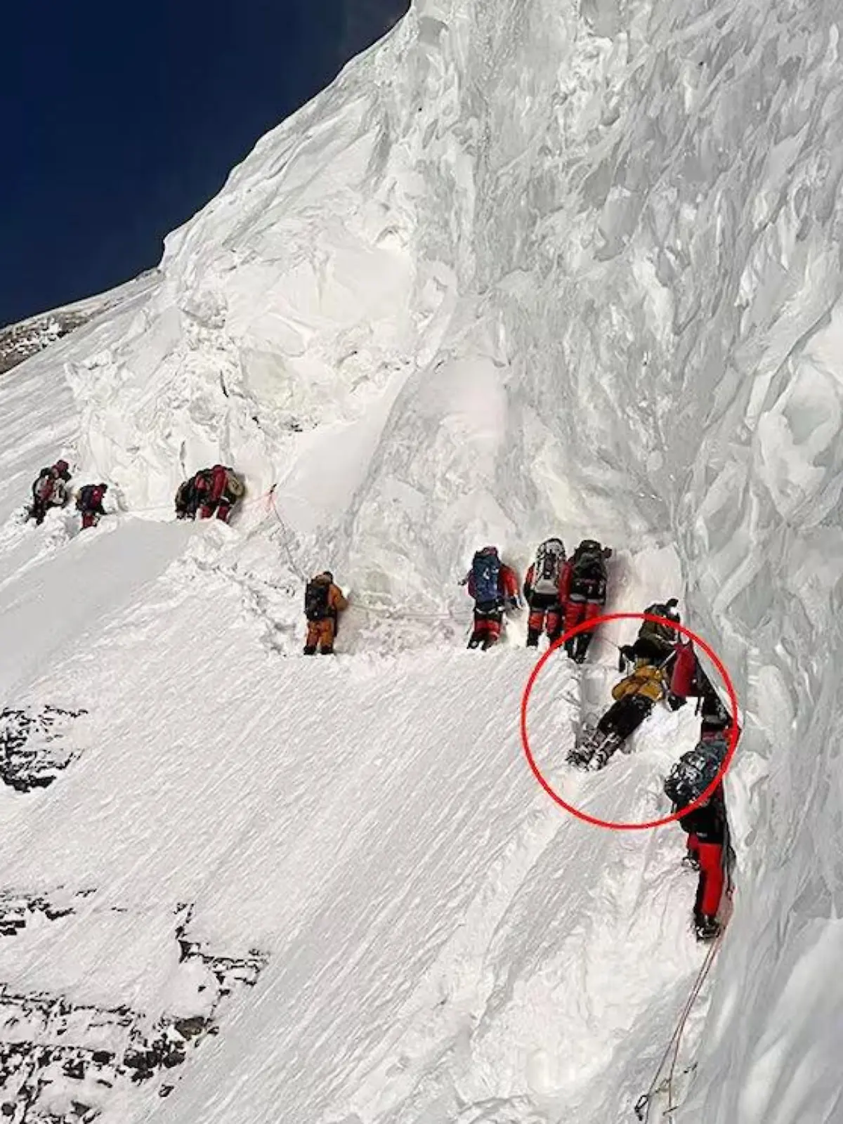 Drohnenaufnahmen zeigen dutzende Bergsteiger auf dem Weg zum Gipfel des K2. Ein Mann liegt flach und fixiert an einer Felswand.