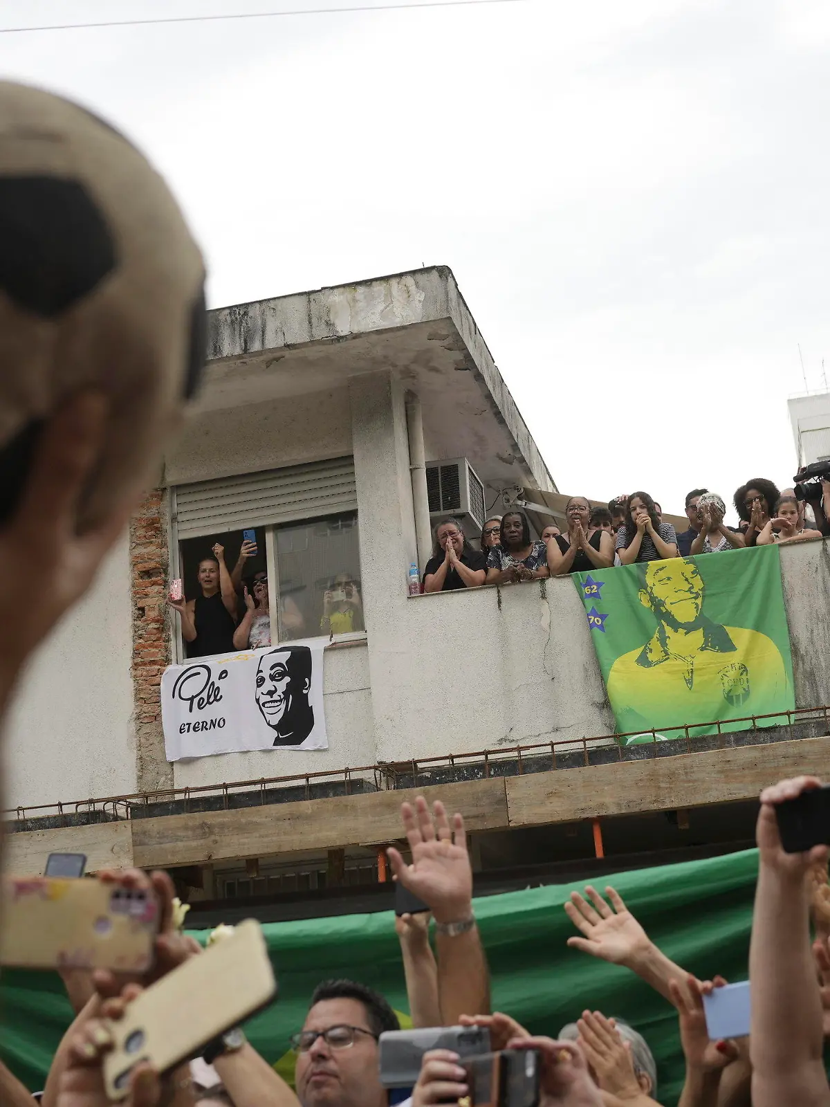 03.01.2023, Brasilien, Santos: Menschen beobachten den Trauerzug für den verstorbenen brasilianischen Fußballstar Pele, der am Haus von Peles Mutter vorbeifährt, wo Mitglieder seiner Familie auf dem Balkon stehen, als sein Leichnam vom Stadion Vila Belmiro, wo er aufgebahrt wurde zum Friedhof gebracht wird. Der Ausnahme-Fußballer Pele starb am 29.12.2022 im Alter von 82 Jahren in Sao Paulo. Foto: Matias Delacroix/AP/dpa +++ dpa-Bildfunk +++