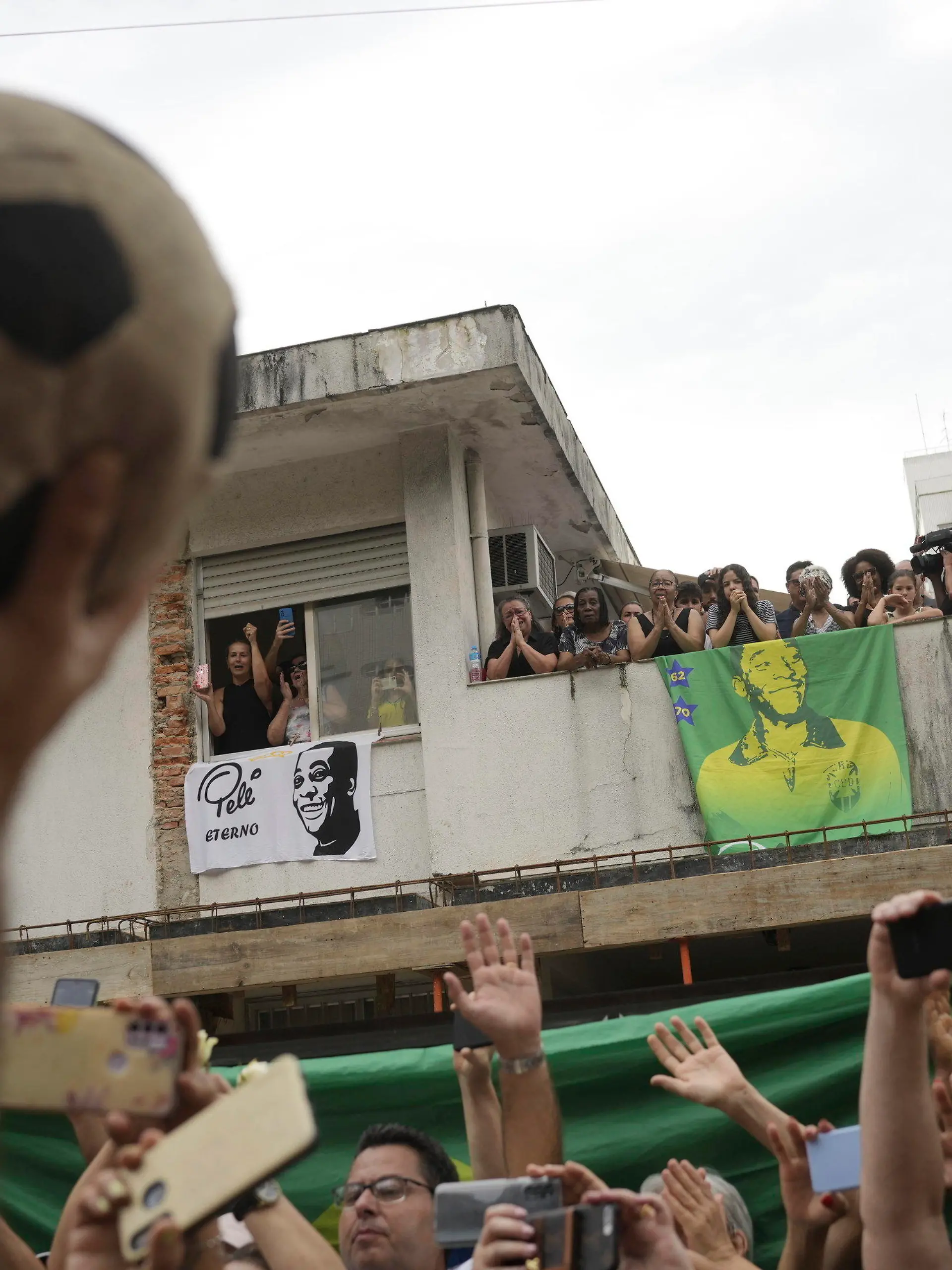 03.01.2023, Brasilien, Santos: Menschen beobachten den Trauerzug für den verstorbenen brasilianischen Fußballstar Pele, der am Haus von Peles Mutter vorbeifährt, wo Mitglieder seiner Familie auf dem Balkon stehen, als sein Leichnam vom Stadion Vila Belmiro, wo er aufgebahrt wurde zum Friedhof gebracht wird. Der Ausnahme-Fußballer Pele starb am 29.12.2022 im Alter von 82 Jahren in Sao Paulo. Foto: Matias Delacroix/AP/dpa +++ dpa-Bildfunk +++