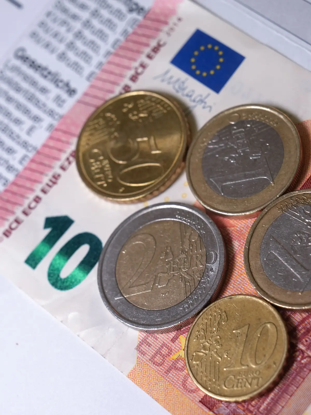 Euro- und Centmünzen liegen auf einer Entgeltabrechnung und auf einem 10-Euro-Schein