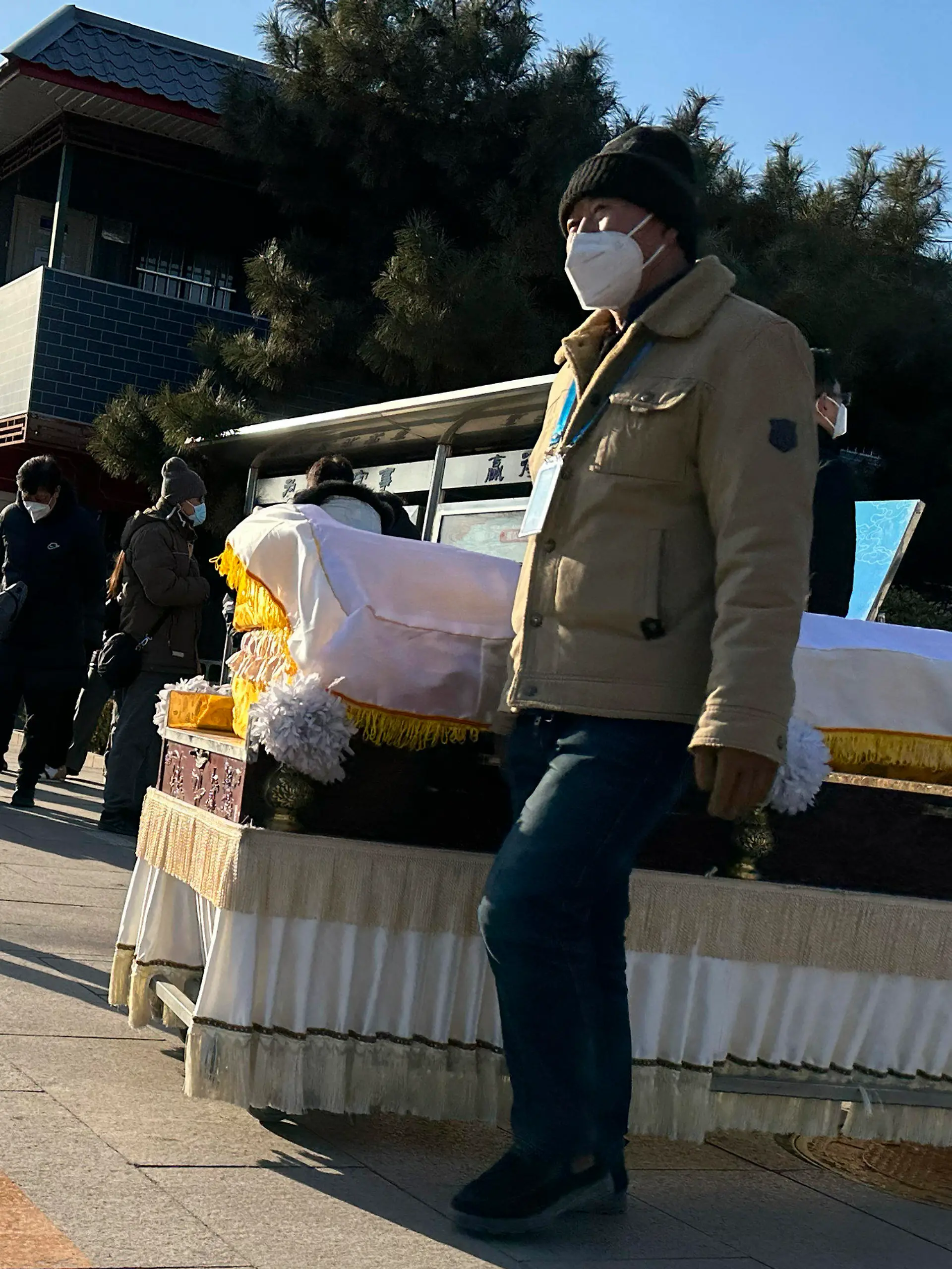 31.12.2022, China, Beijing: Arbeiter schieben einen Sarg vor ein Krematorium. China hat Anfang dieses Monats viele seiner strengen Corona-Beschränkungen aufgehoben, so dass sich das Virus rasch ausbreiten konnte. Die Zahl der Einäscherungen ist um ein Vielfaches gestiegen. Viele Bestattungsinstitute sind ausgelastet und bitten die Familien die Beerdigungen zu verschieben. Foto: Ng Han Guan/AP/dpa +++ dpa-Bildfunk +++