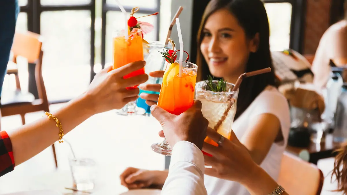 Beautiful and cheerful Asian woman cheering up for toast and celebration with friends in bar - focus on glasses