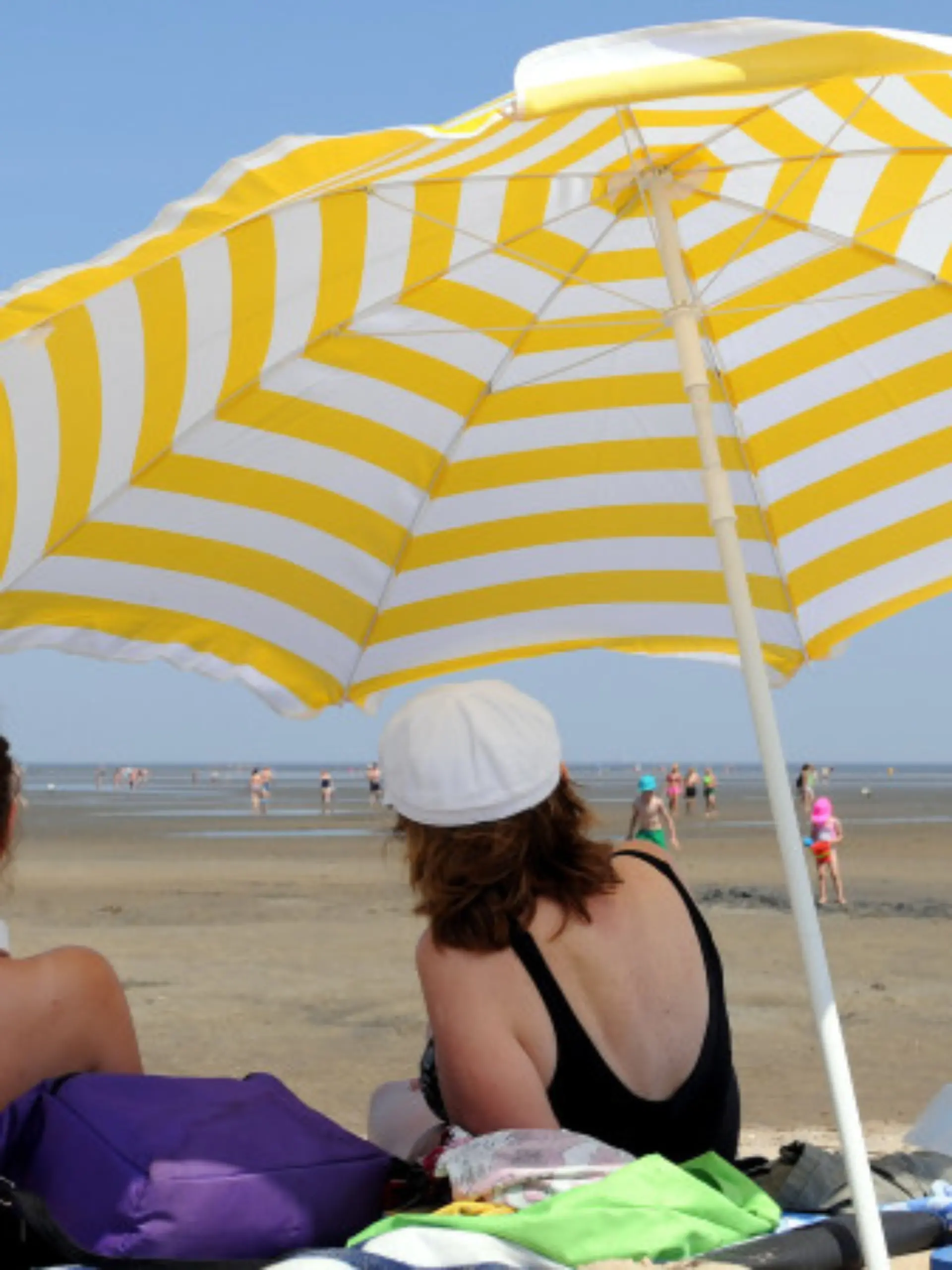 ARCHIV - Zwei Nordseeurlauberinnen liegen am 19.07.2014 bei Ebbe und Lufttemperaturen über 30 Grad Celsius unter ihrem Sonnenschirm am Strand von Cuxhaven-Döse (Niedersachsen). Foto: Ingo Wagner/dpa (zu lni "Wetter lässt Touristik-Branche strahlen - Küste gut gebucht" vom 22.07.2014) +++(c) dpa - Bildfunk+++