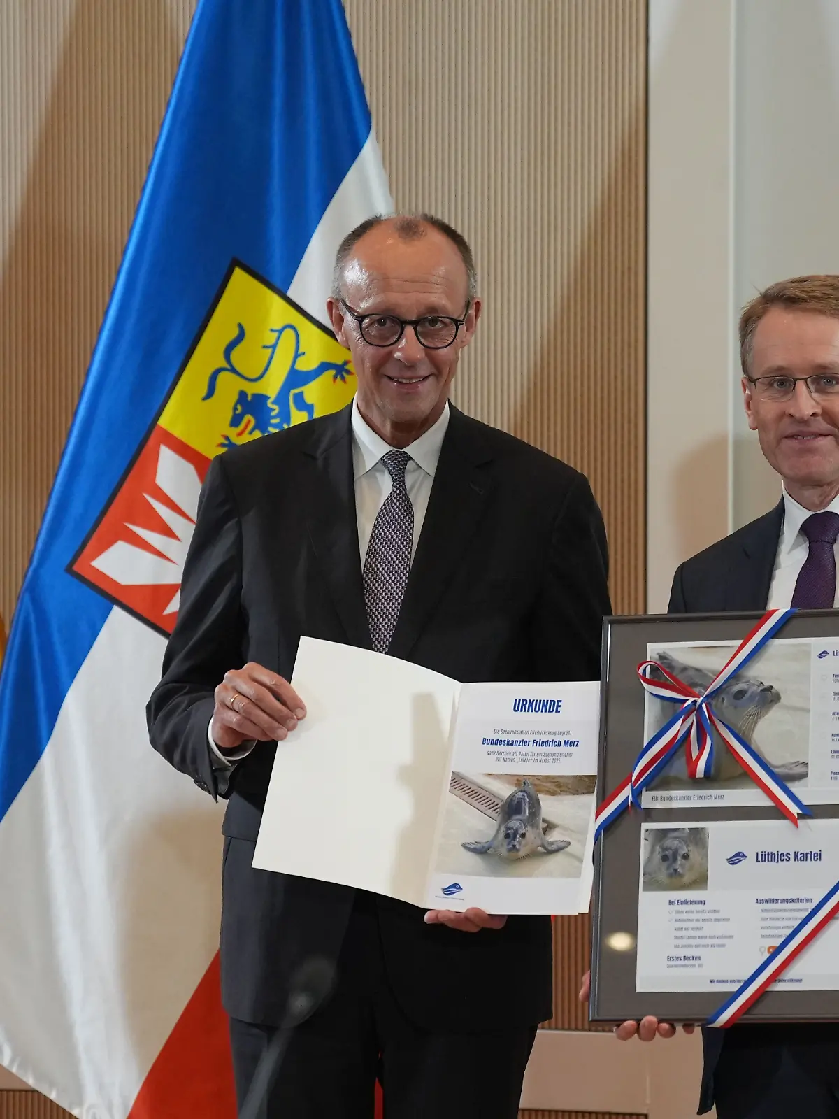 Bundeskanzler Friedrich Merz (CDU) erhält von Schleswig-Holsteins Ministerpräsident Daniel Günther (CDU) im Rathaus von Husum eine Urkunde für die Patenschaft der Robbe „Lütje” in der Seehundstation Friedrichskoog. 