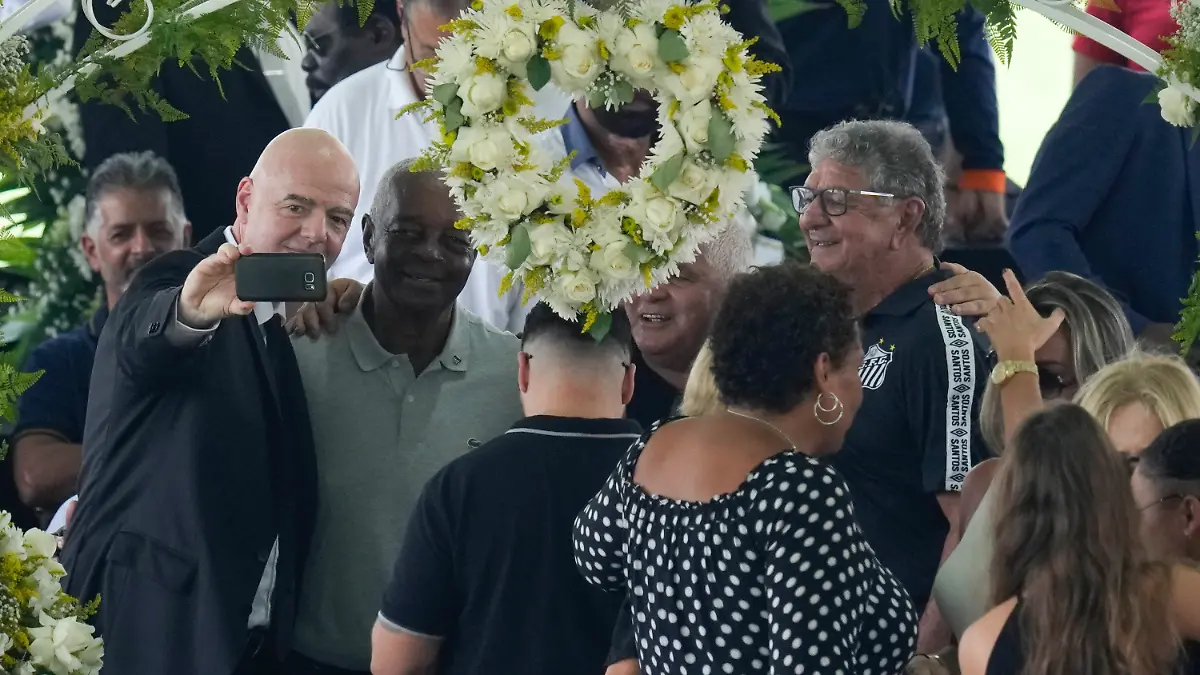 FIFA President Gianni Infantino, left, takes a selfie with Lima, a former Santos soccer player, and others, during the wake of the late Brazilian soccer great Pele, who lies in state, below, at Vila Belmiro stadium in Santos, Brazil, Monday, Jan. 2, 2023. (AP Photo/Andre Penner)