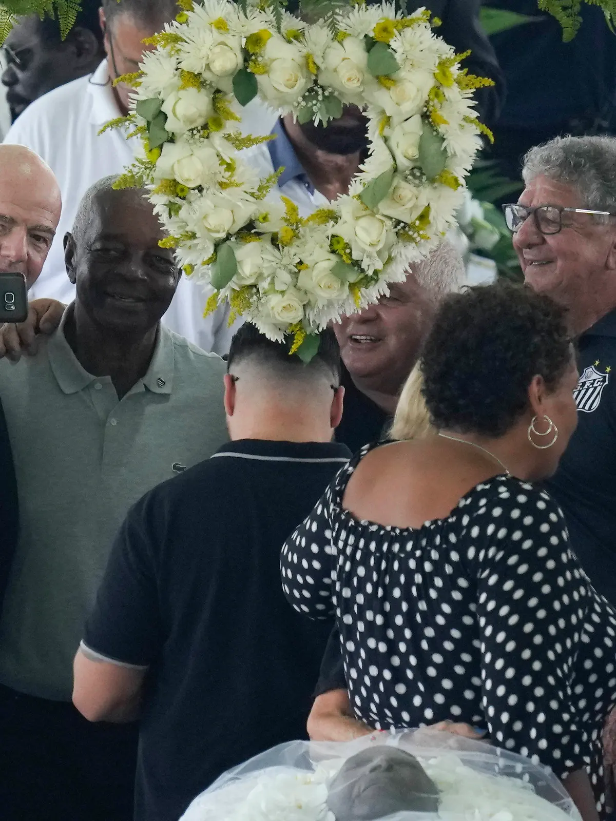 FIFA President Gianni Infantino, left, takes a selfie with Lima, a former Santos soccer player, and others, during the wake of the late Brazilian soccer great Pele, who lies in state, below, at Vila Belmiro stadium in Santos, Brazil, Monday, Jan. 2, 2023. (AP Photo/Andre Penner)