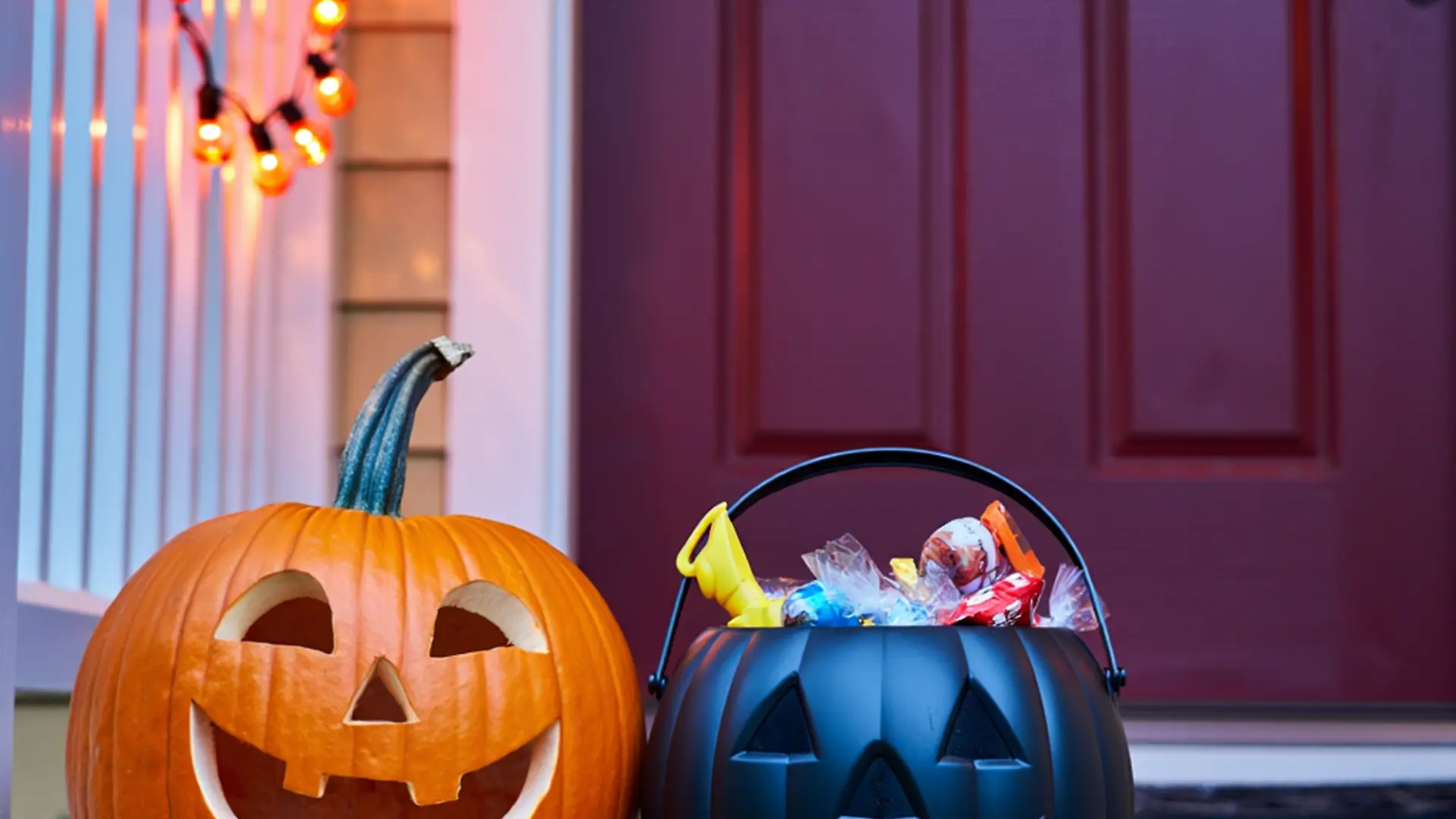 Fröhliches Halloween! Ein geschnitzter Kürbis und ein Süßigkeiteneimer stehen auf der Verandatreppe.