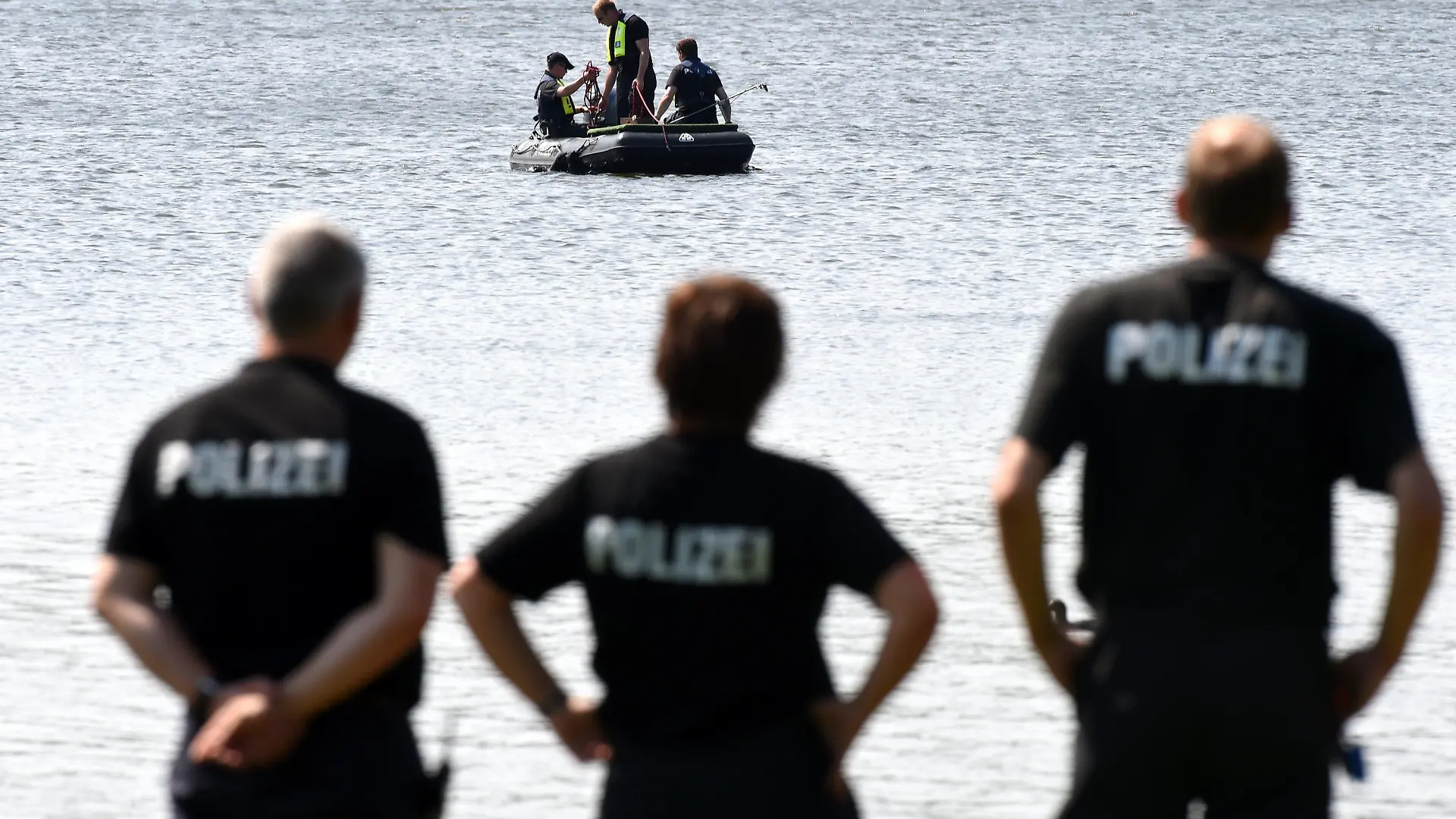 Polizeibeamte beobachten am 21.07.2014 am Badesee Selker Noor bei Schleswig (Schleswig-Holstein) ihre Kollegen, die zuvor eine Leiche geborgen haben. Ob es sich bei der Toten um die seit Samstag vermisste 47 Jahre alte Frau handelt, ist noch nicht bestätigt. Foto: Carsten Rehder/dpa +++(c) dpa - Bildfunk+++