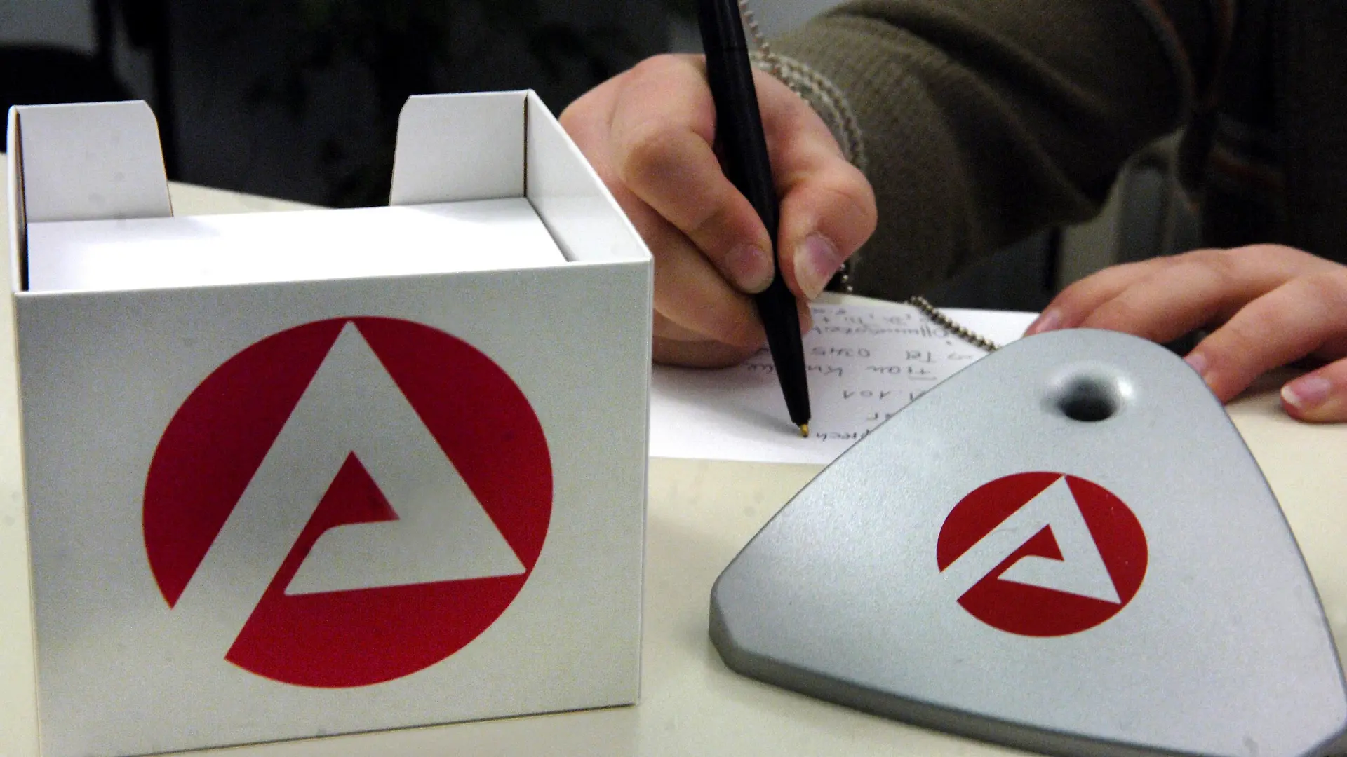 Eine Mitarbeiterin der Agentur für Arbeit in Halle schreibt am Dienstag (17.05.2005) in ihrer Behörde hinter einem Zettelkasten und einem Kugelschreiberbehälter, die mit dem neuen Logo versehen sind. Als eine der ersten Agenturen für Arbeit in Deutschland hat die Arbeitsagentur in Halle mit dem Anbringen des neuen Logos ihre Umstrukturierung zum Kundenzentrum abgeschlossen. Das neue Logo mit weißem A auf rotem Untergrund soll nach Angaben der Nürnberger Bundesagentur für Arbeit gegenüber dem alten Logo mit rotem A auf weißen Untergrund das Erscheinungsbild für die Arbeitssuchenden freundlicher und offener gestalten. Das neue Logo, dessen Entwicklung rund 100.000 Euro gekostet haben soll, hatte bei seiner Vorstellung Diskussionen ausgelöst. Foto: Waltraud Grubitzsch/lah +++(c) dpa - Report+++
