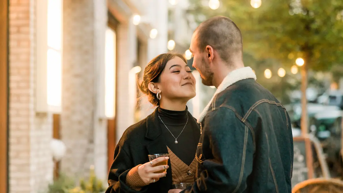Couple in love about to kiss outside a coffee shop in the city. Young man and woman holding a tea about to kiss outdoors in a winter evening.
