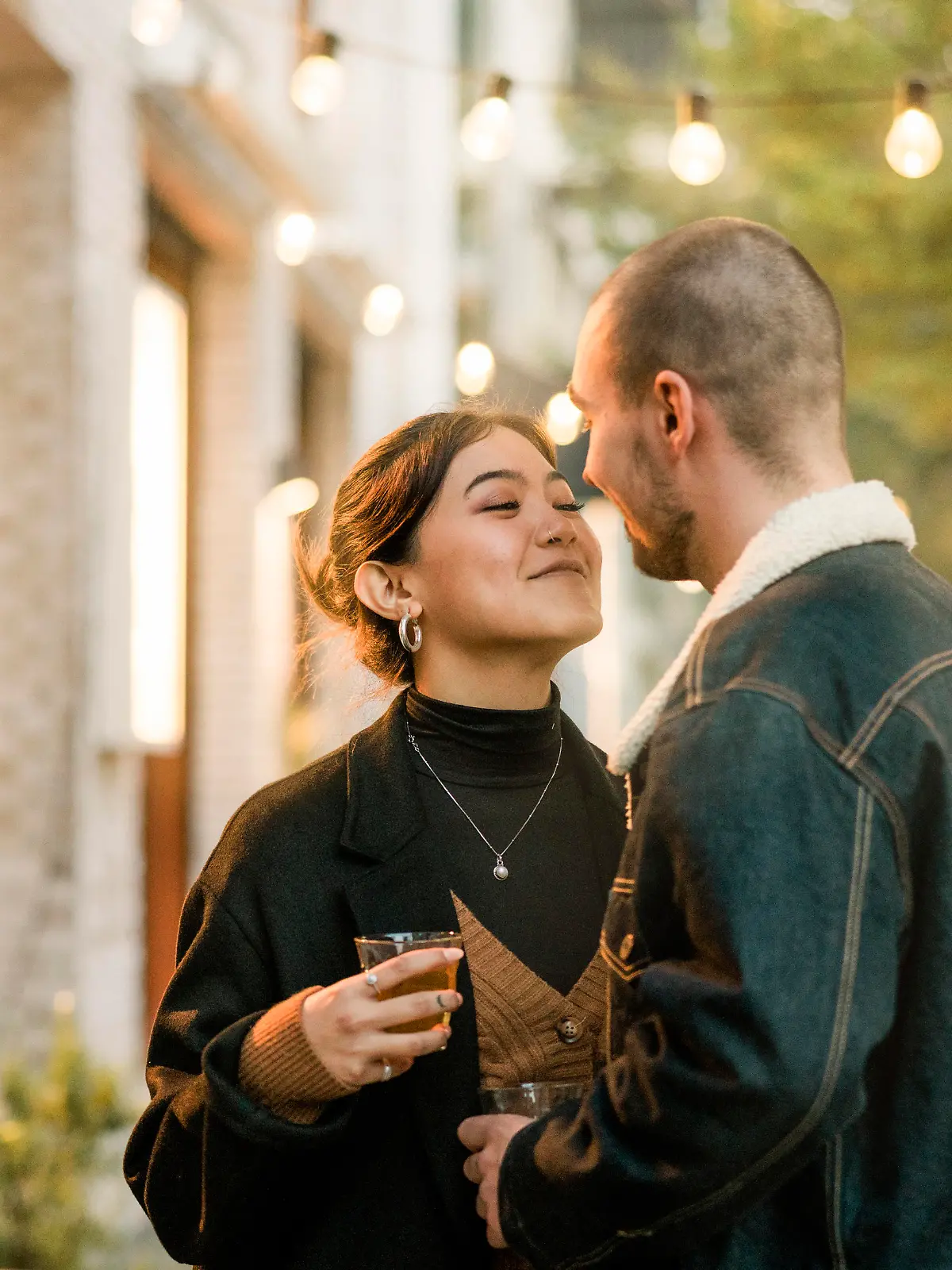 Couple in love about to kiss outside a coffee shop in the city. Young man and woman holding a tea about to kiss outdoors in a winter evening.