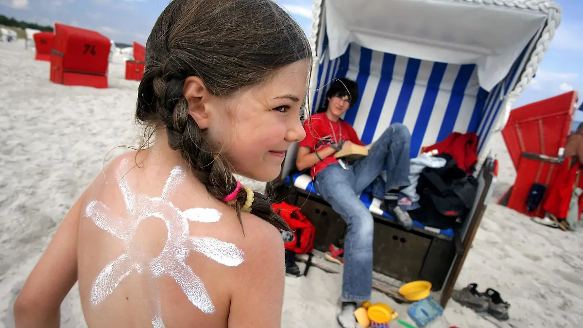 Die sechsjährige Bentje steht am Donnerstag (03.08.2006) mit einer Sonne aus Sonnencreme am Strand von Prerow auf der Halbinsel Darß. Bei wechselhaftem Wetter mit Temperaturen um die 25 Grad legen viele Touristen und Tagesgäste nach den vergangenen Hitzewochen erst einmal eine Strandpause ein. Foto: Jens Büttner/lmv +++(c) dpa - Report+++