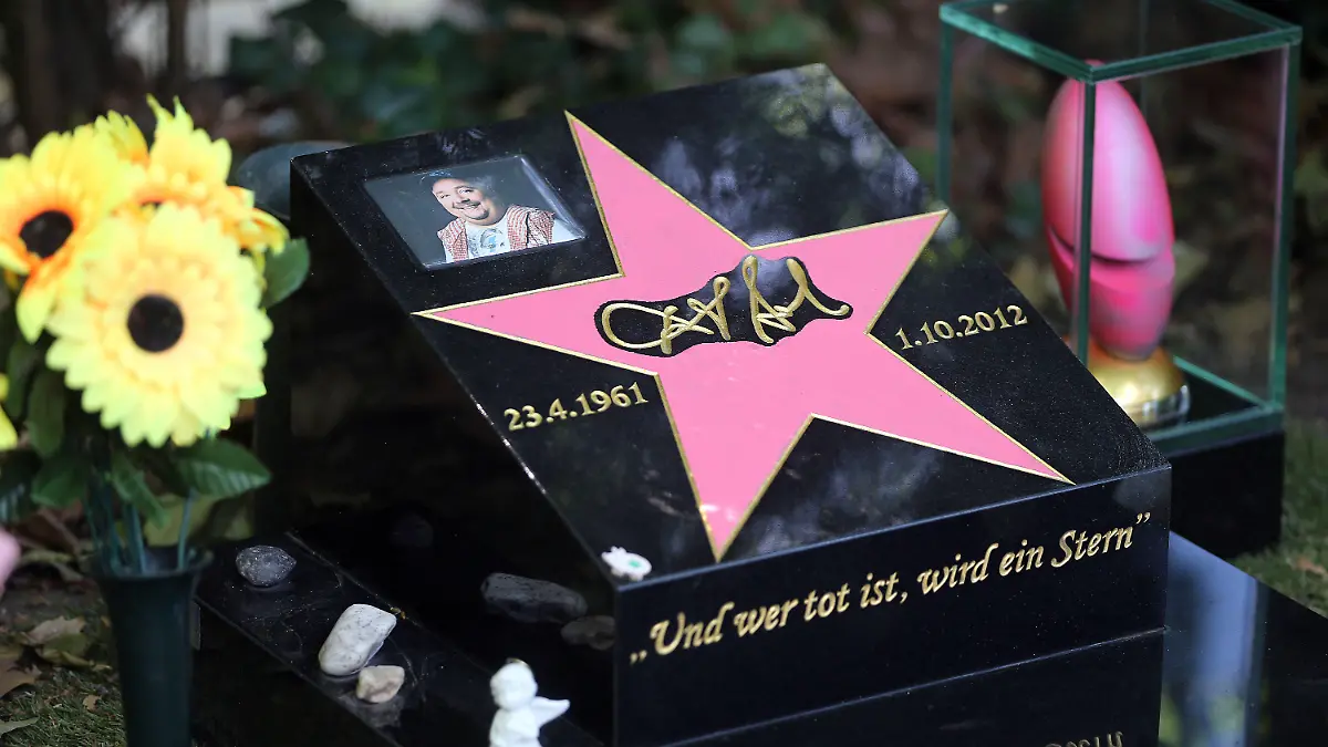 Ein pinkes Ei (r) steht am 18.06.2014 neben dem Grabstein des Schauspielers und Komikers Dirk Bach auf dem Melatenfriedhof in Köln (Nordrhein-Westfalen). Bei dem knalligen Objekt handelt es sich um den Deutschen Comedypreis, den Bachs Kollegin Zietlow ohne ihren verstorbenen Freund im Oktober 2013 zunächst nicht annehmen wollte. Foto: Oliver Berg/dpa (zu dpa: «Knallpink: Comedypreis an Dirk Bachs Grab montiert») +++(c) dpa - Bildfunk+++