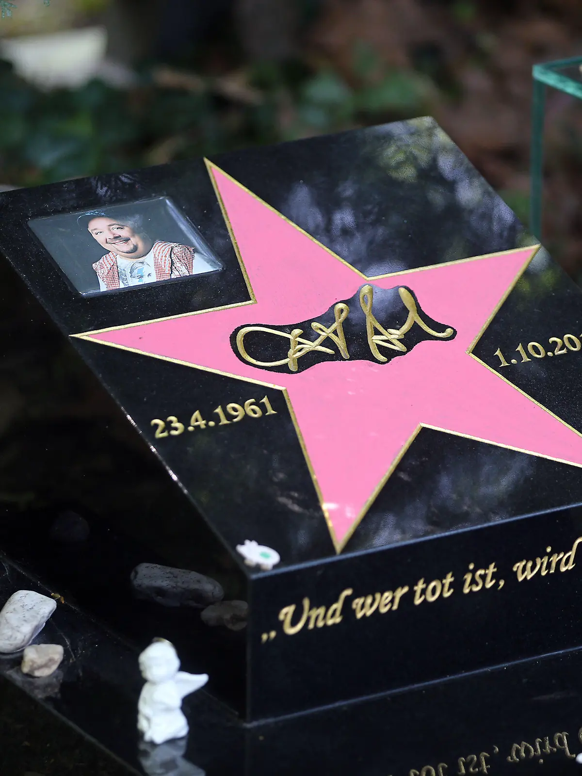 Ein pinkes Ei (r) steht am 18.06.2014 neben dem Grabstein des Schauspielers und Komikers Dirk Bach auf dem Melatenfriedhof in Köln (Nordrhein-Westfalen). Bei dem knalligen Objekt handelt es sich um den Deutschen Comedypreis, den Bachs Kollegin Zietlow ohne ihren verstorbenen Freund im Oktober 2013 zunächst nicht annehmen wollte. Foto: Oliver Berg/dpa (zu dpa: «Knallpink: Comedypreis an Dirk Bachs Grab montiert») +++(c) dpa - Bildfunk+++