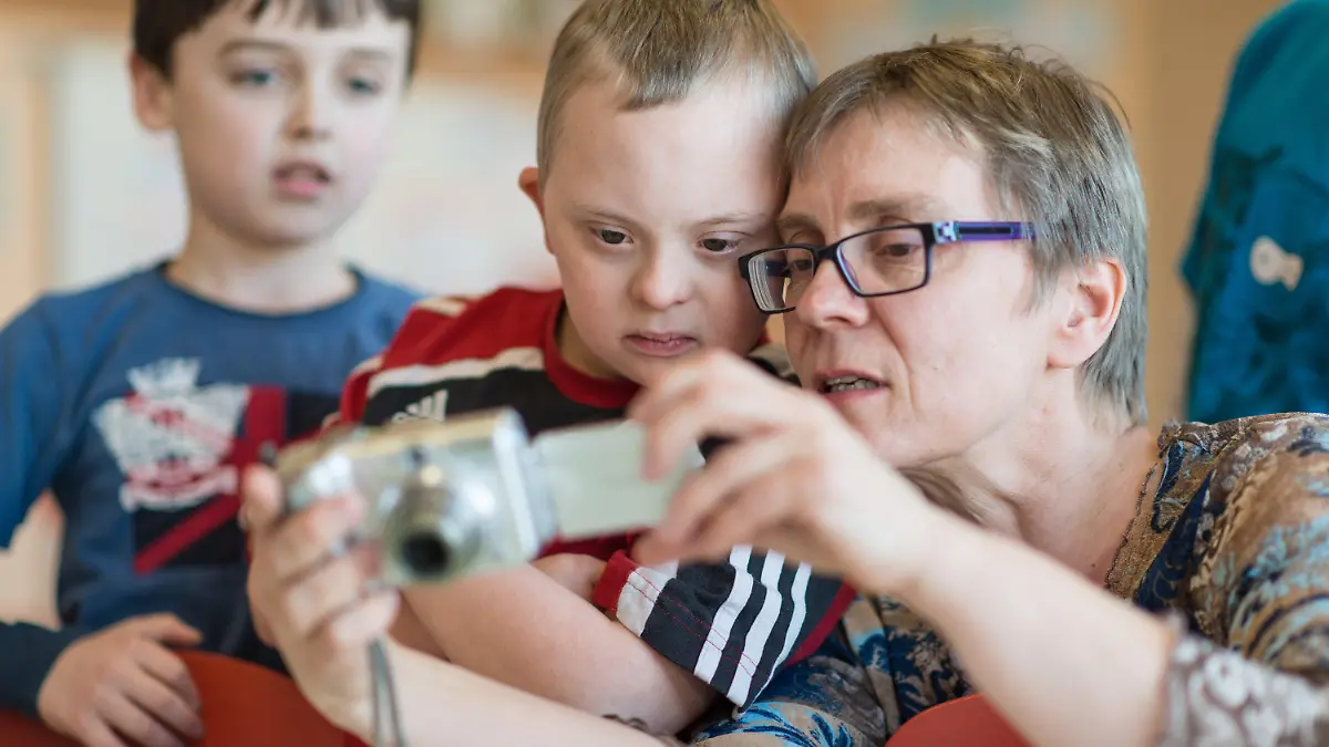 Der Viertklässler Henri (M), ein Kind mit Down-Syndrom, betrachtet am 27.03.2014 in Walldorf (Baden-Württemberg) in der Schillerschule zusammen mit seiner Mutter Kirsten Erhardt und Mitschülern die Fotos einer Digitalkamera. Vier Jahre lang hat Henri gemeinsam mit seinen Klassenkameraden gelernt und gespielt. Nach der Grundschule möchte der Elfjährige mit Down-Syndrom gern wie seine Freunde aus Walldorf im Rhein-Neckar-Kreis aufs Gymnasium wechseln. Er wäre eines der ersten behinderten Kinder an einem Südwest-Gymnasium, das anders als seine Mitschüler das angestrebte Bildungsziel nicht erreichen kann. Foto: Uwe Anspach/dpa (zu lsw-Korr: «Offene Fragen der Inklusion: Down-Syndrom-Kind will aufs Gymi» vom 07.04.2014) +++(c) dpa - Bildfunk+++