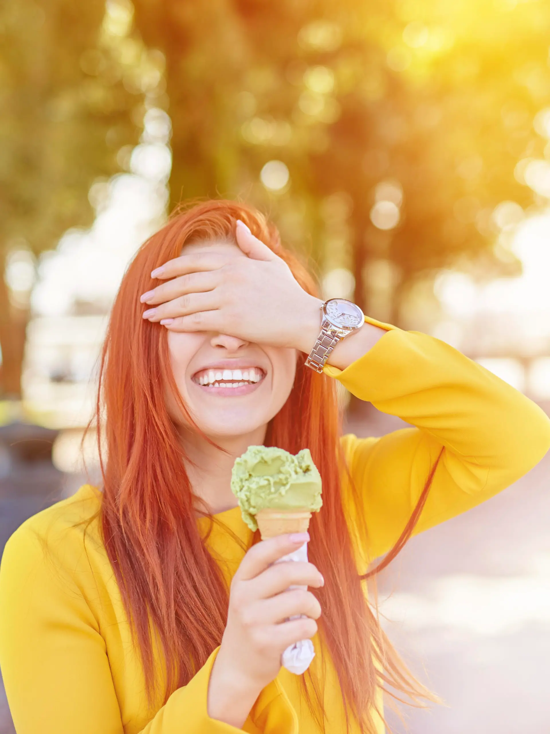 happy woman outdoors playing with her icecream and covering face, big toothy smile.