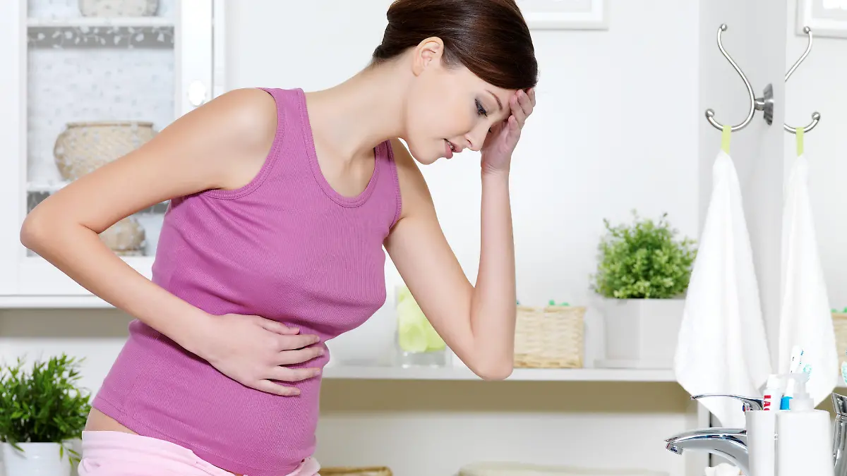 Pregnant woman with strong pain of stomach and nausea sitting in bathroom