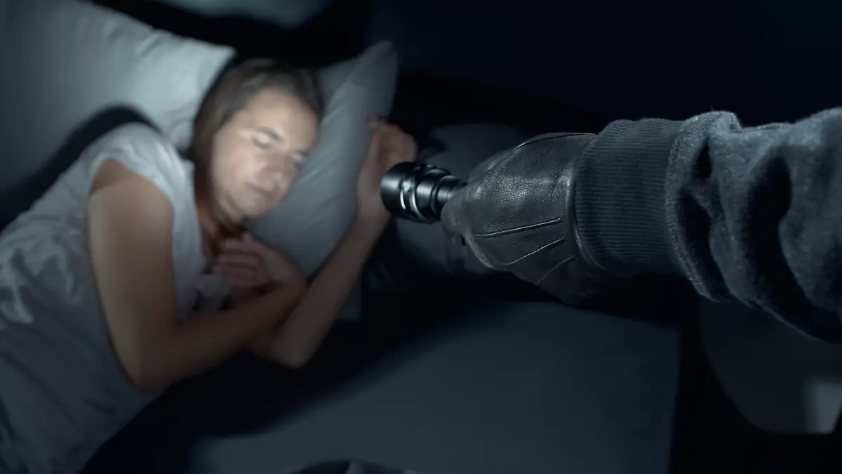 Thief threatening a woman at night in her home, he is pointing a flashlight at her face and she is sleeping in bed
