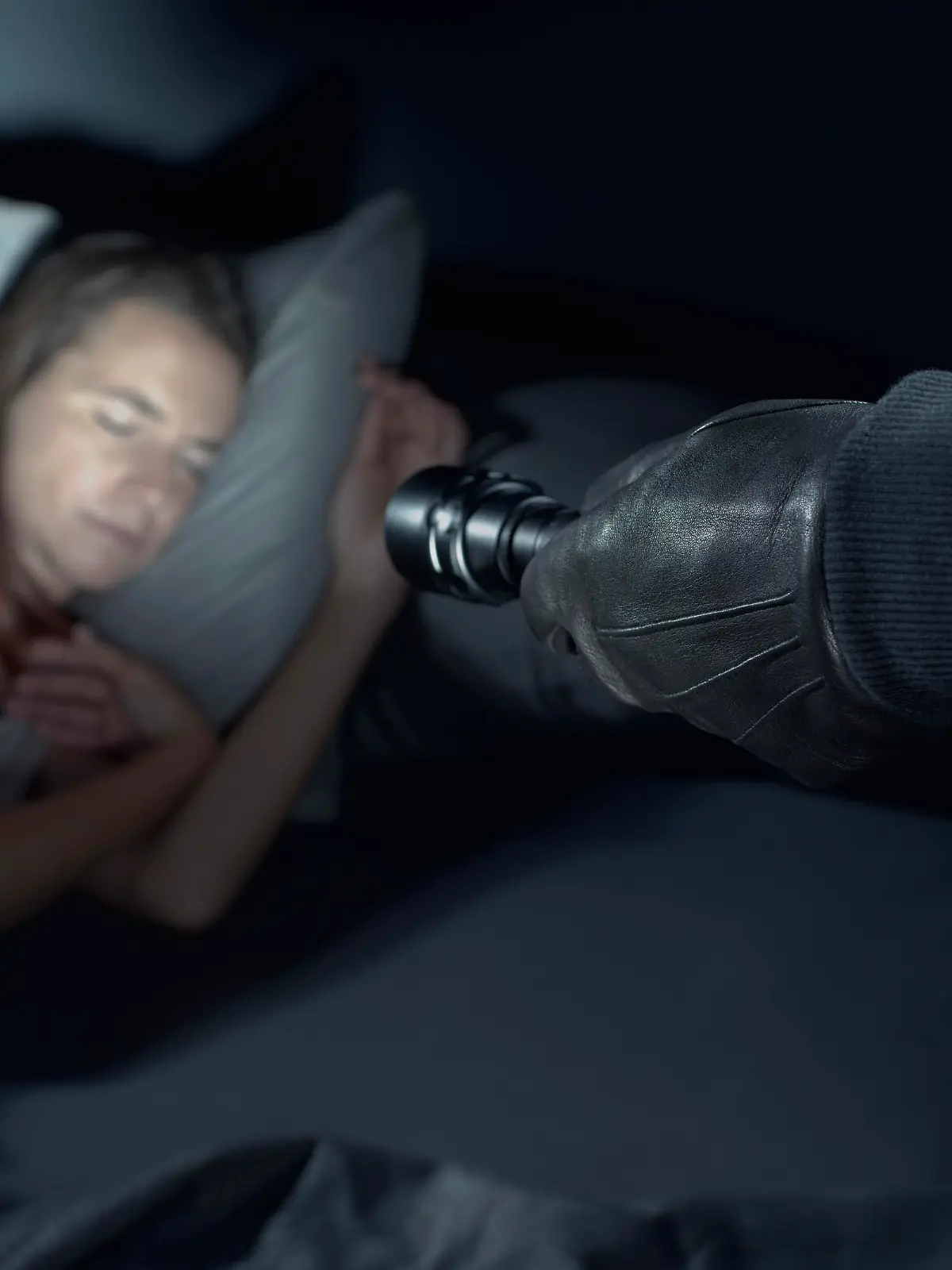 Thief threatening a woman at night in her home, he is pointing a flashlight at her face and she is sleeping in bed