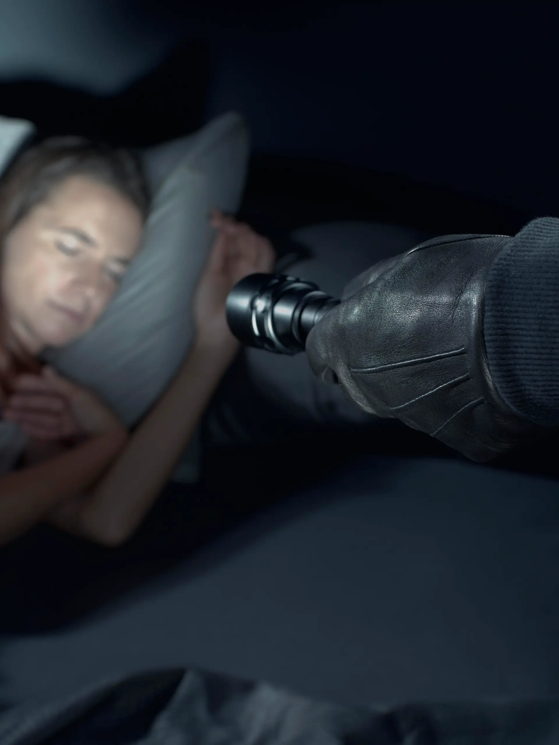 Thief threatening a woman at night in her home, he is pointing a flashlight at her face and she is sleeping in bed