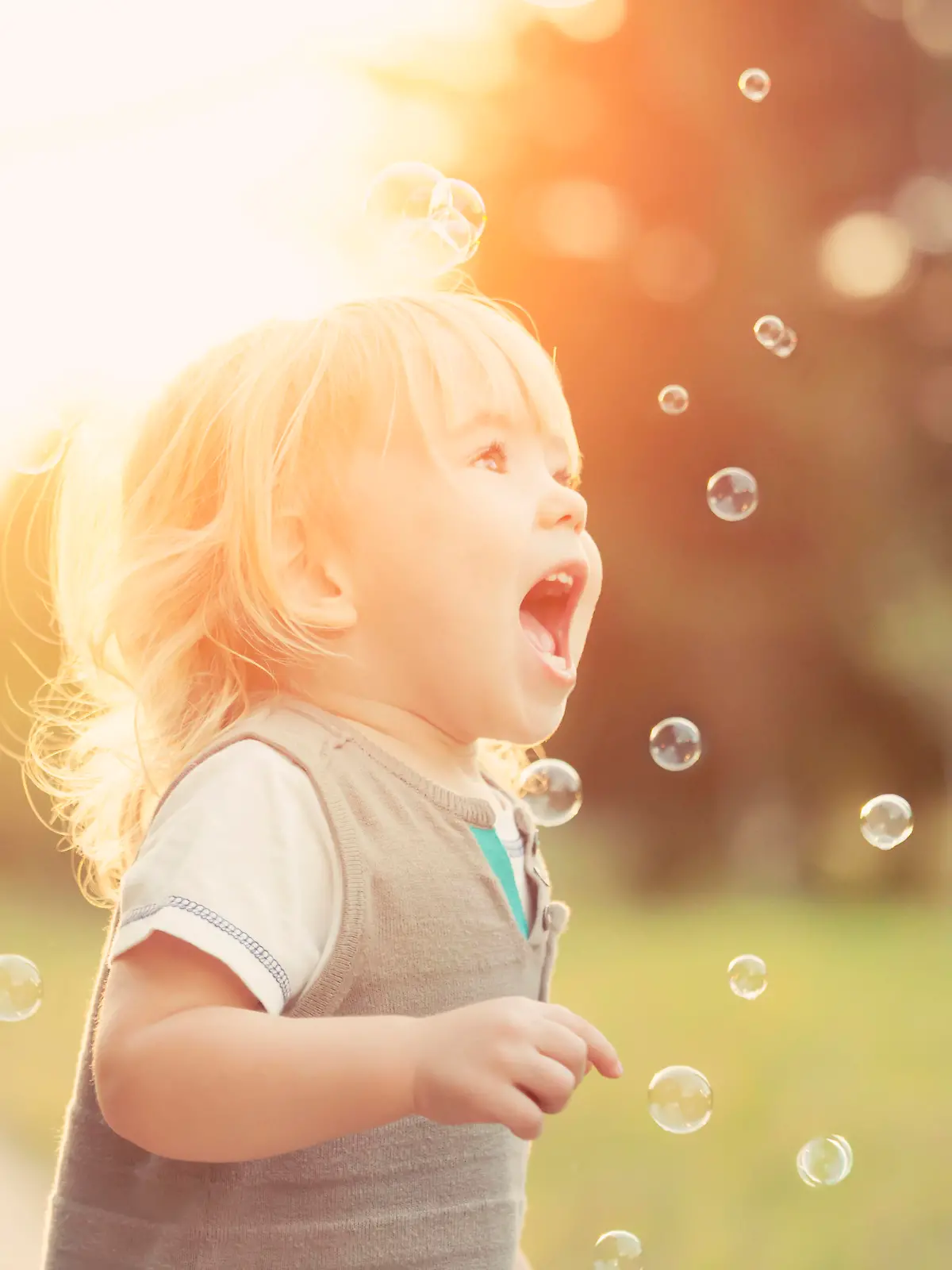 Little blonde boy playing with soap bubbles in a park.
