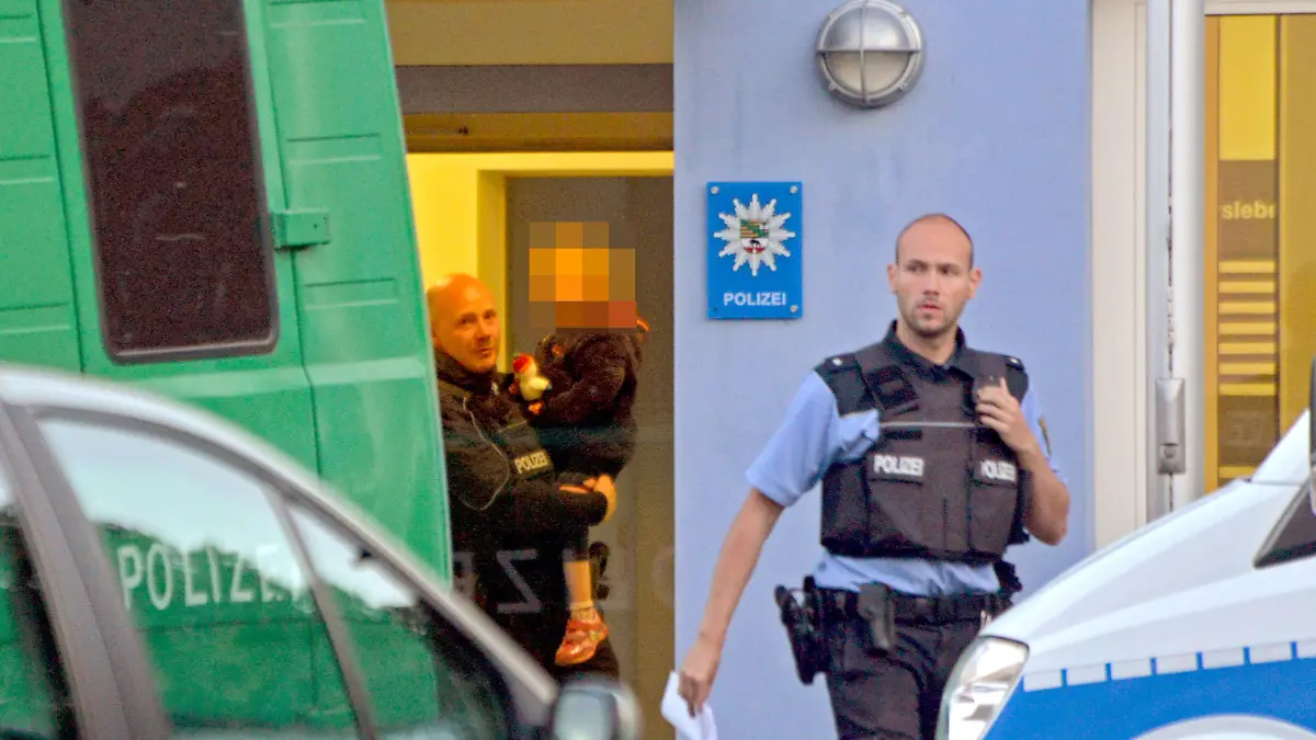 Ein Polizist trägt am 03.05.2014 in Aschersleben (Sachsen-Anhalt) ein Kind auf dem Arm, welches bei einer Razzia zugegen war. Der Polizei ist ein Schlag gegen ein bundesweit operierendes Pädophilen-Netz gelungen. Bei der Razzia in Aschersleben sind zehn Männer im Alter zwischen 22 und 60 Jahren und eine 57 Jahre alte Frau festgenommen worden, die zum engsten Kreis des Netzwerkes gehören sollen. Foto: Frank Gehrmann/dpa +++(c) dpa - Bildfunk+++