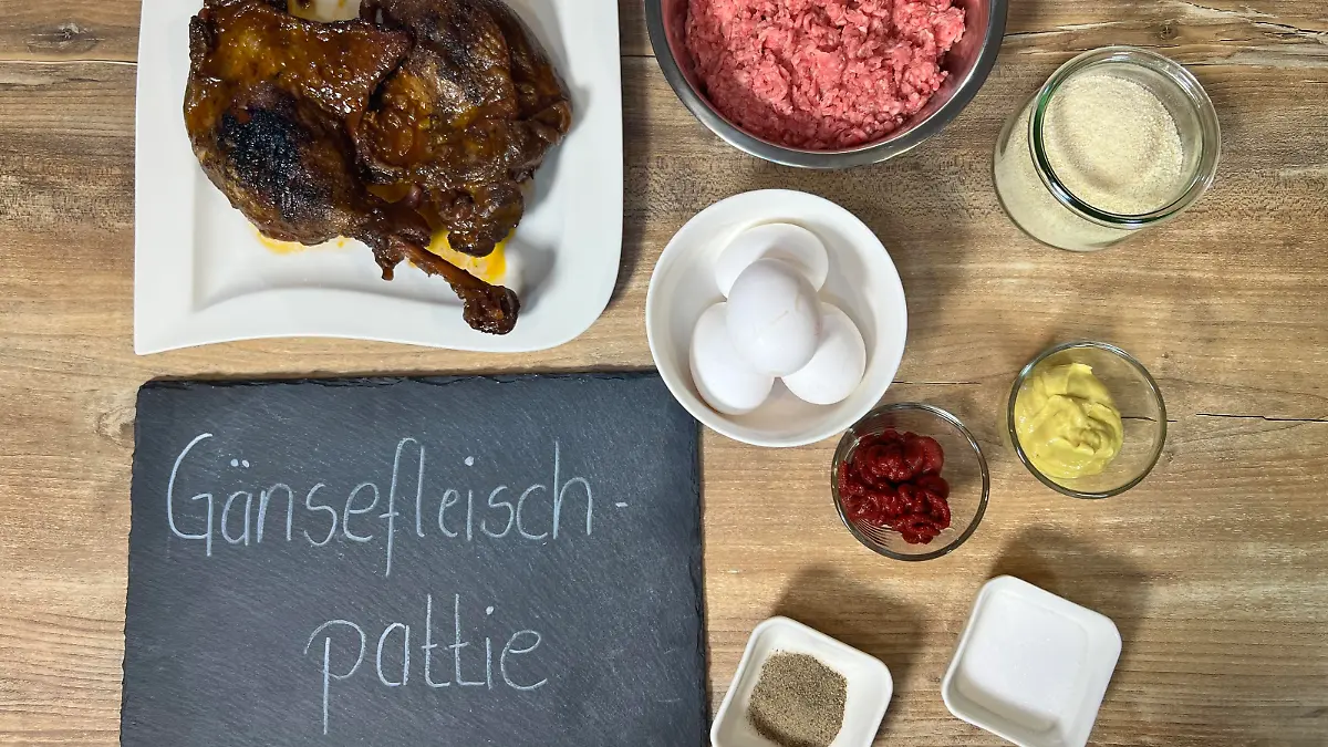 Auf diesen Bild sehen Sie alle zutaten, diese man für Gänsefleischpattie benötigt und eine Tafel auf der unteren linken Seite mit der Aufschrift: Gänsefleischpattie
