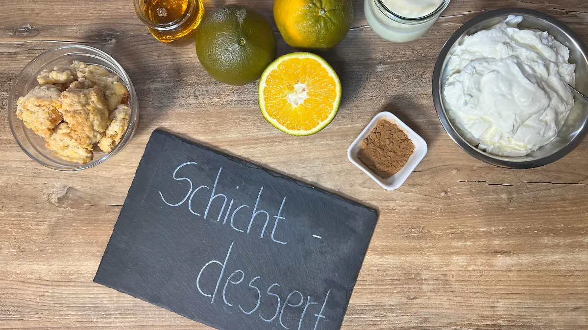 Auf diesen Bild sehen Sie alle Zutaten für das Schichtdessert und in der unteren Mitte liegt eine Schiefertafel mit der Aufschrift: Schichtdessert