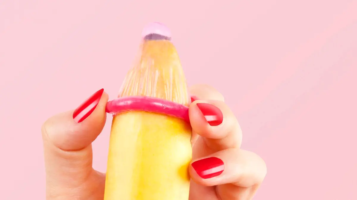 Female hand with red fingernails puts on a condom onto a banana. Safe sex concept. || Modellfreigabe vorhanden