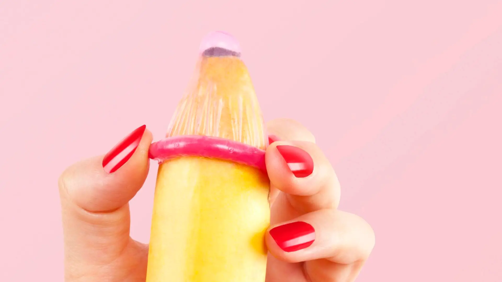Female hand with red fingernails puts on a condom onto a banana. Safe sex concept. || Modellfreigabe vorhanden