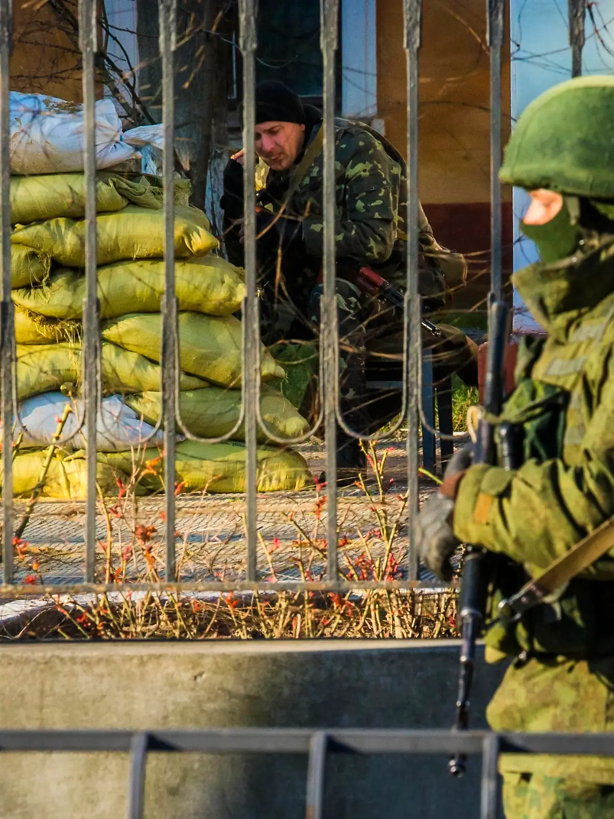 A Ukrainian soldier (L) sits near sandbags at his military base as an armed man, believed to be a Russian soldier, stands guard in Simferopol March 19, 2014. Defying Ukrainian protests and Western sanctions, Russian President Vladimir Putin signed a treaty in Moscow on Tuesday making Crimea part of Russia again, but said he did not plan to seize any other regions of Ukraine.  REUTERS/Thomas Peter (UKRAINE - Tags: POLITICS MILITARY)